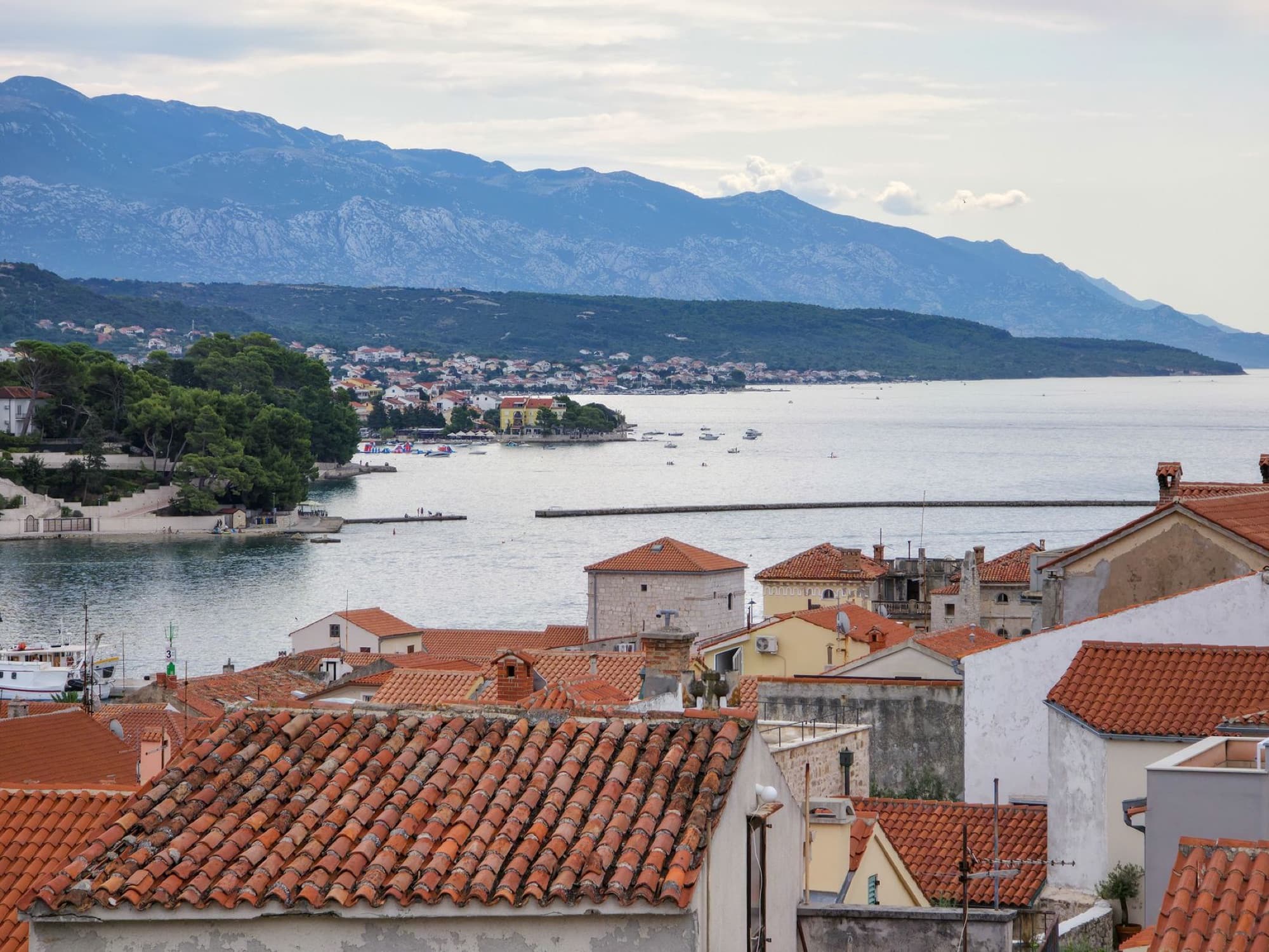 A picturesque view of Island of Rab's coastline with terra-cotta rooftops and distant mountains.