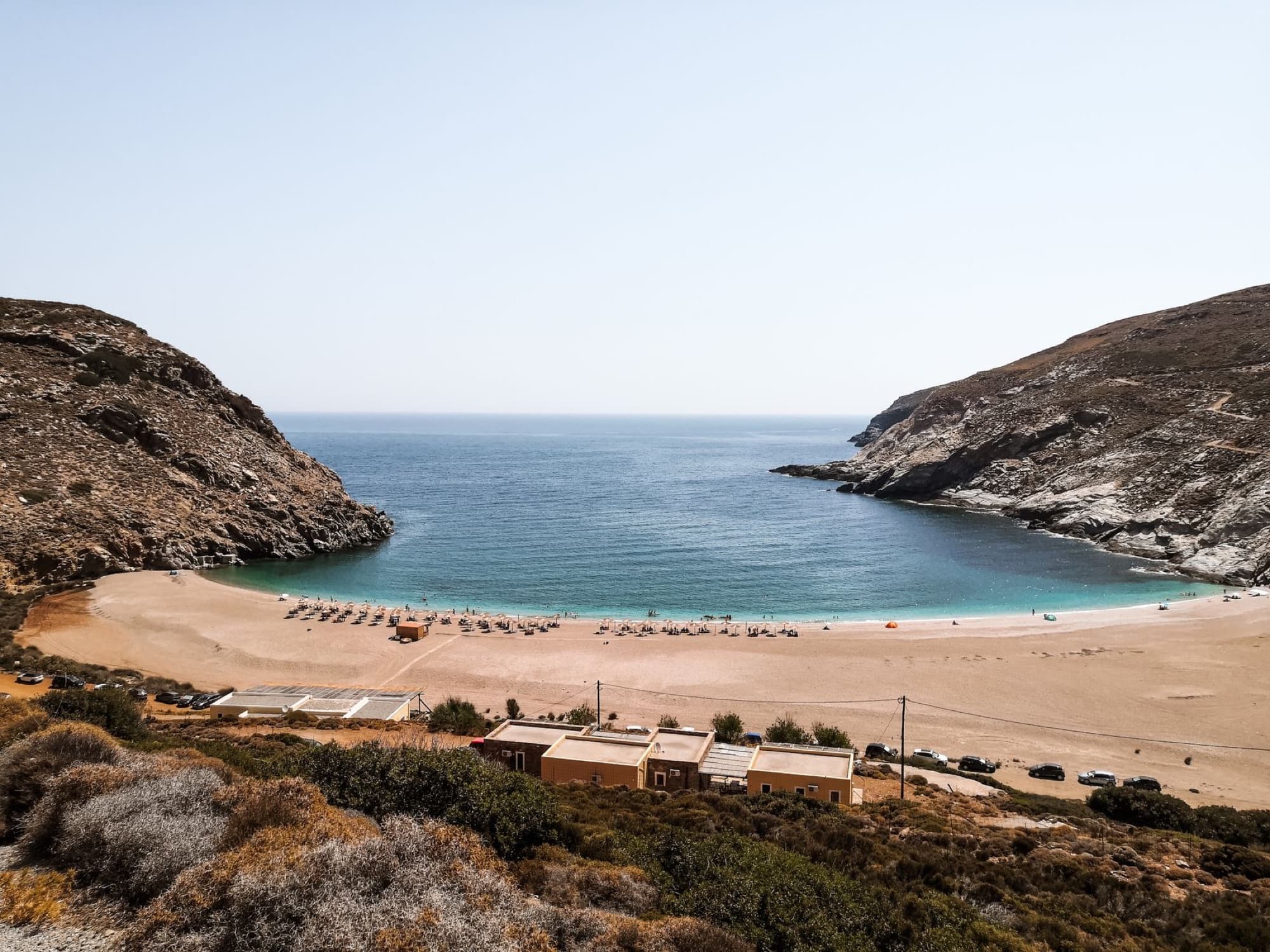 A stunning aerial view of a tranquil beach cove in Andros, Greece, with clear blue waters and sandy shores.