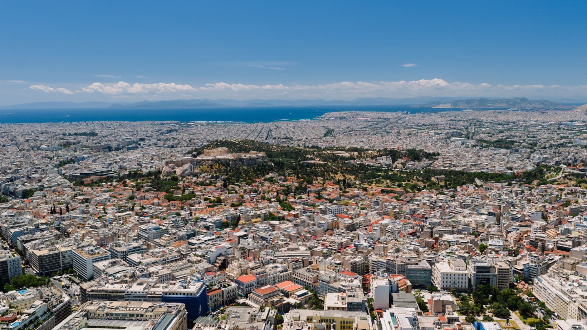 A breathtaking aerial view of Athens, Greece, featuring the Acropolis amid the vast cityscape under a clear blue sky.