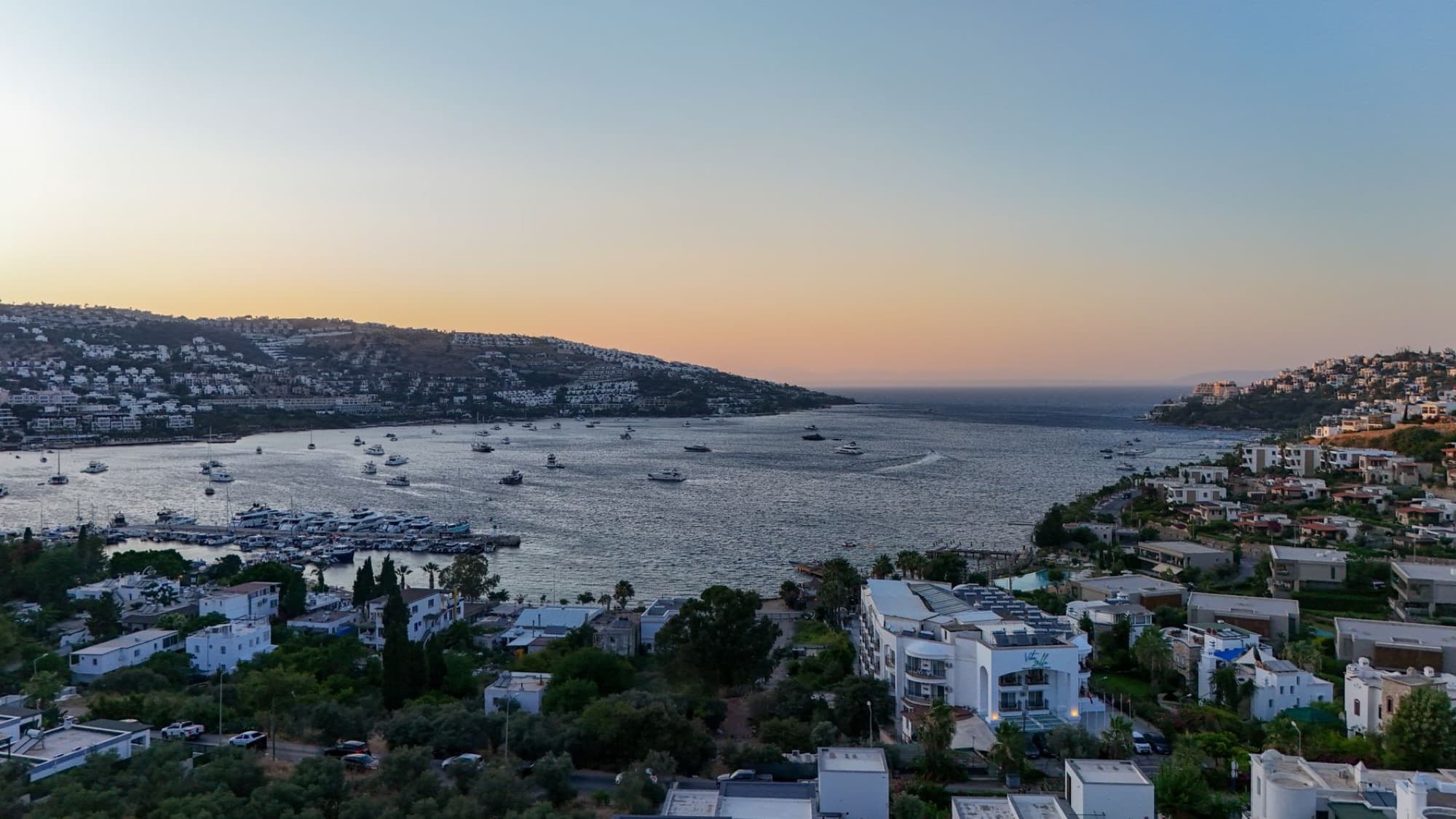 Scenic aerial view of Bodrum's coastline with boats and houses at sunset, showcasing tranquil scenery.