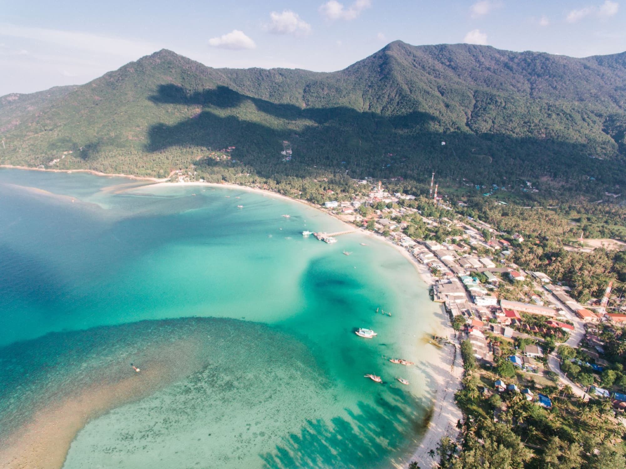 Stunning aerial shot of a tropical island with mountains and clear blue waters.