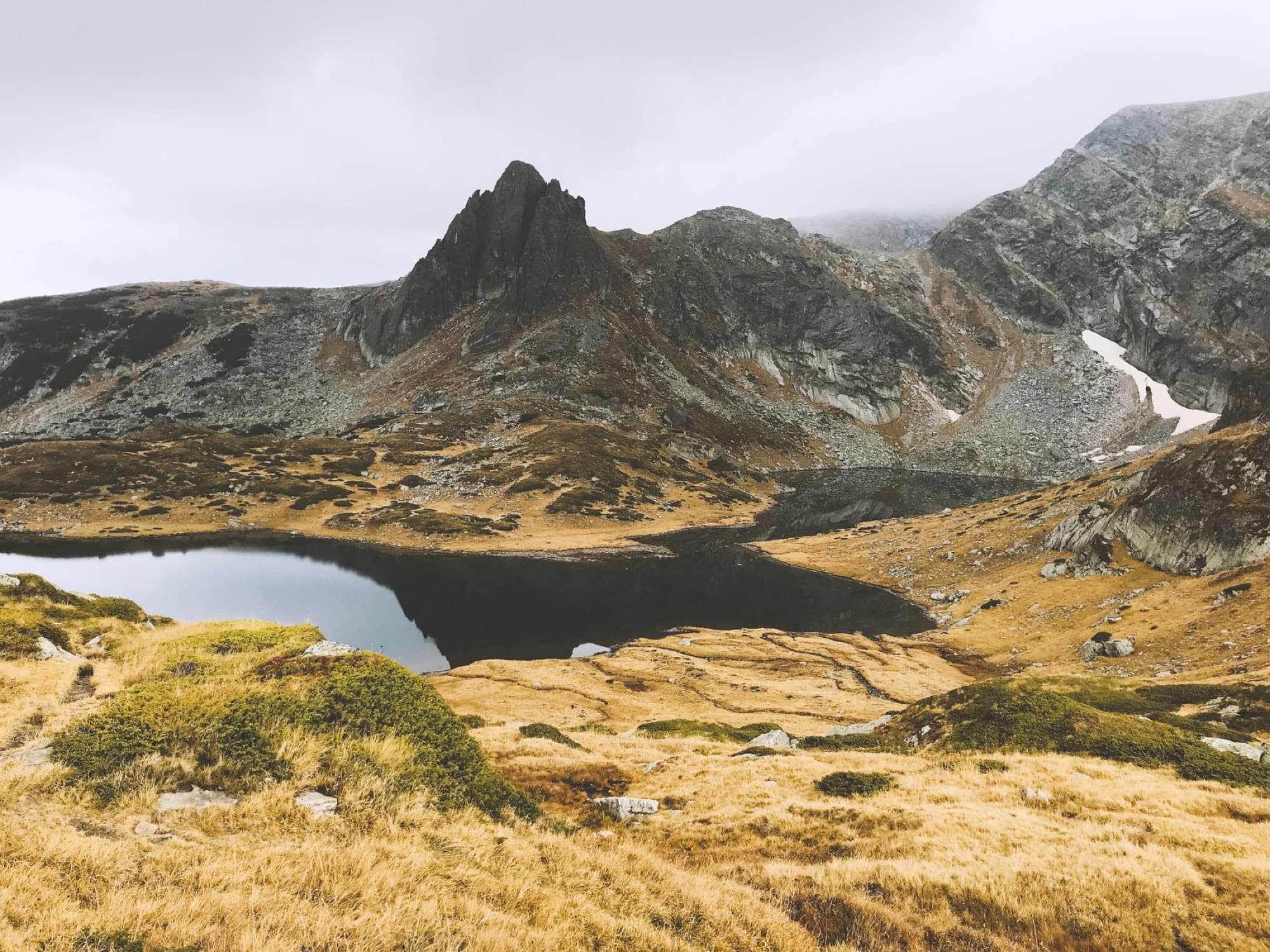 Scenic view of a mountain lake surrounded by rocky terrain and misty peaks in Bulgaria.