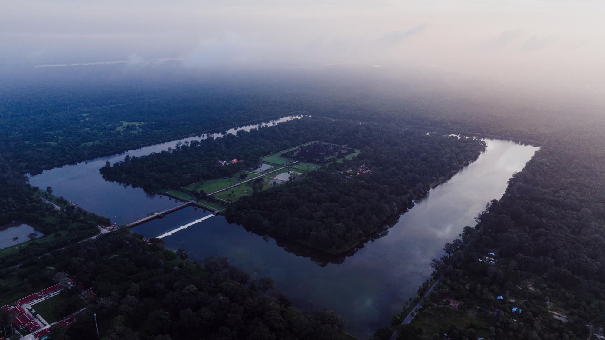 Aerial view of Angkor Wat in Cambodia shrouded in mist with a surrounding moat.