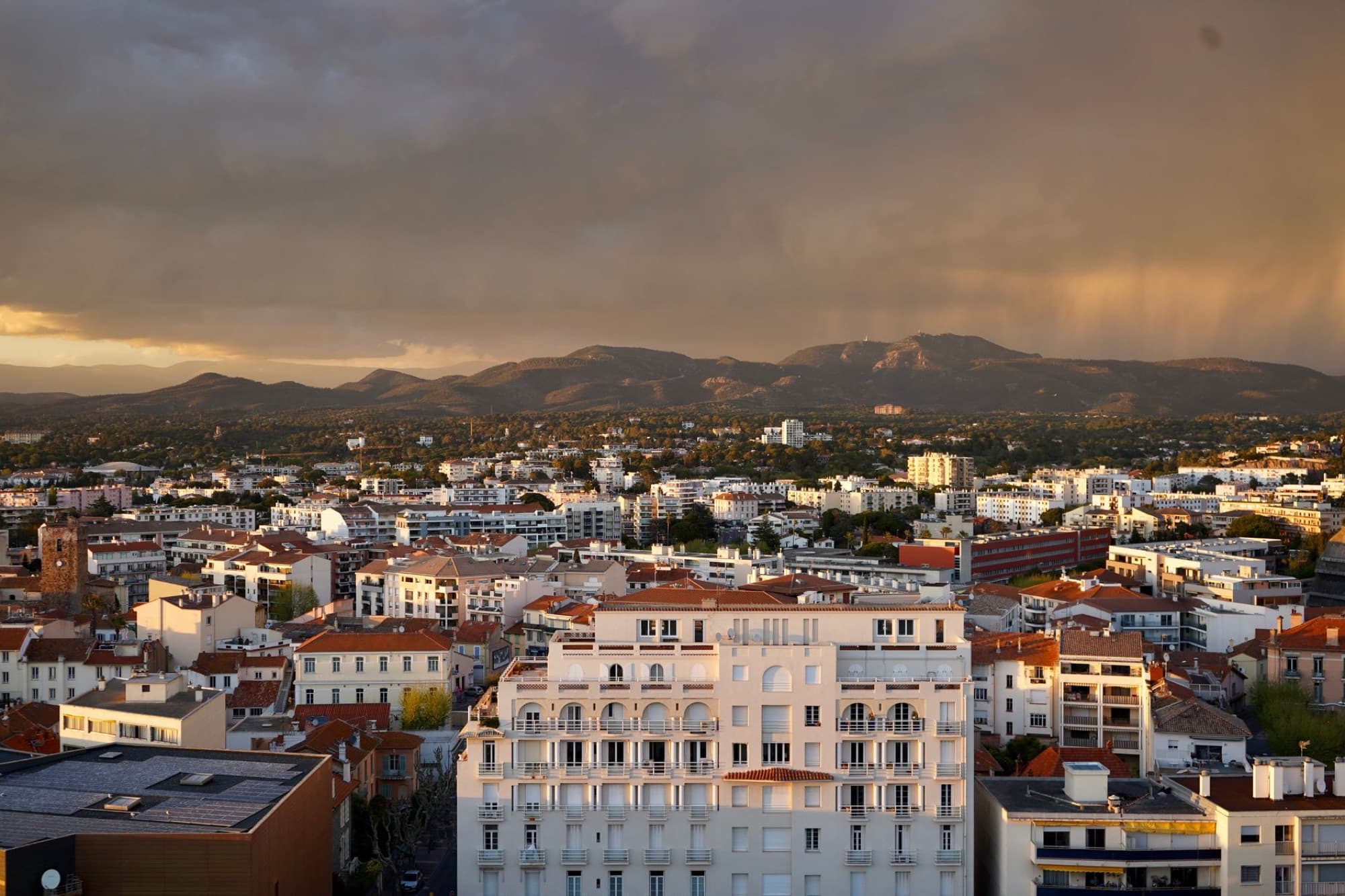 A vibrant cityscape with mountains during sunset, displaying urban architecture against a scenic backdrop.