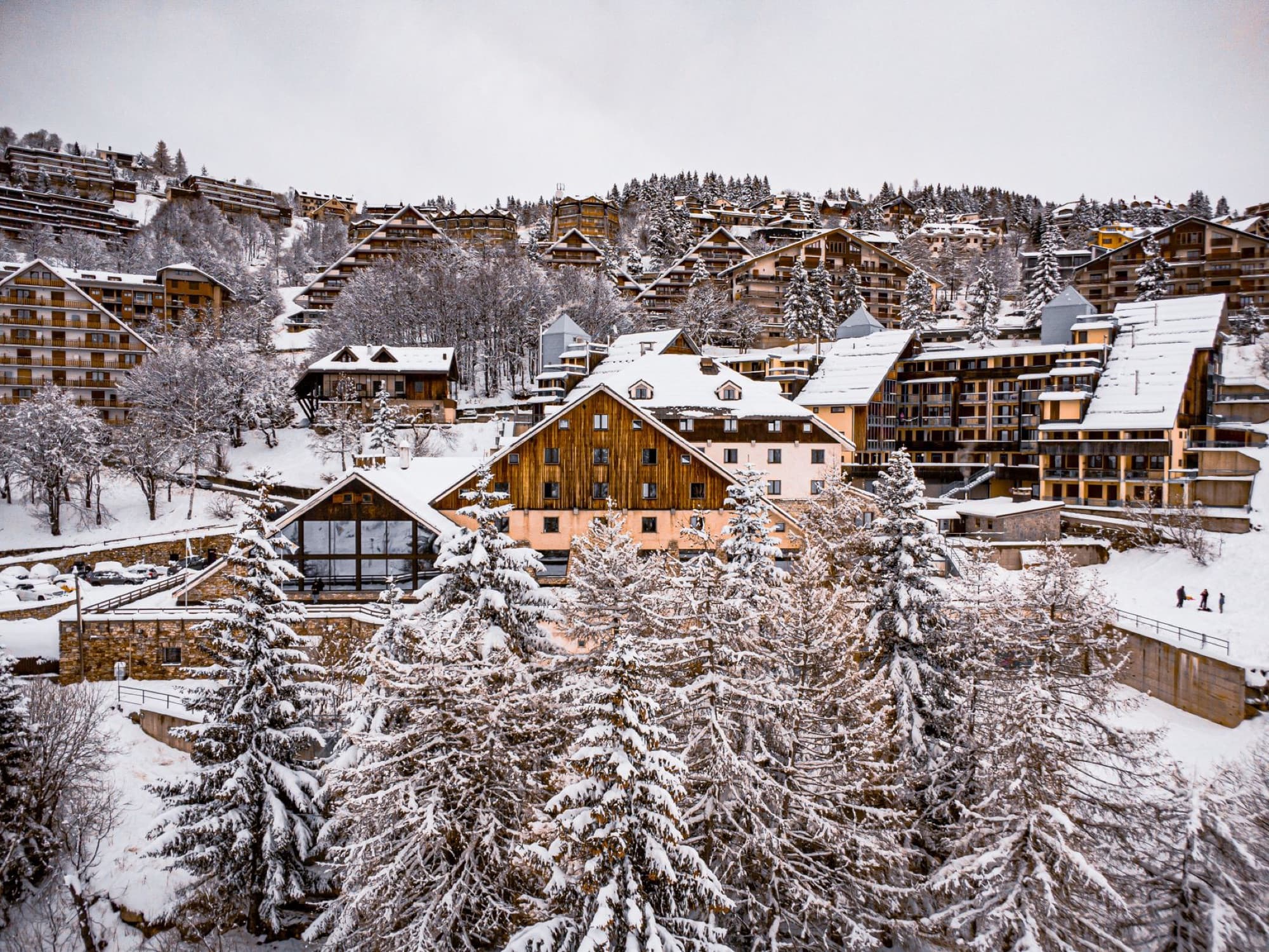A picturesque aerial of a snow-covered mountain village surrounded by evergreen trees and buildings in winter.