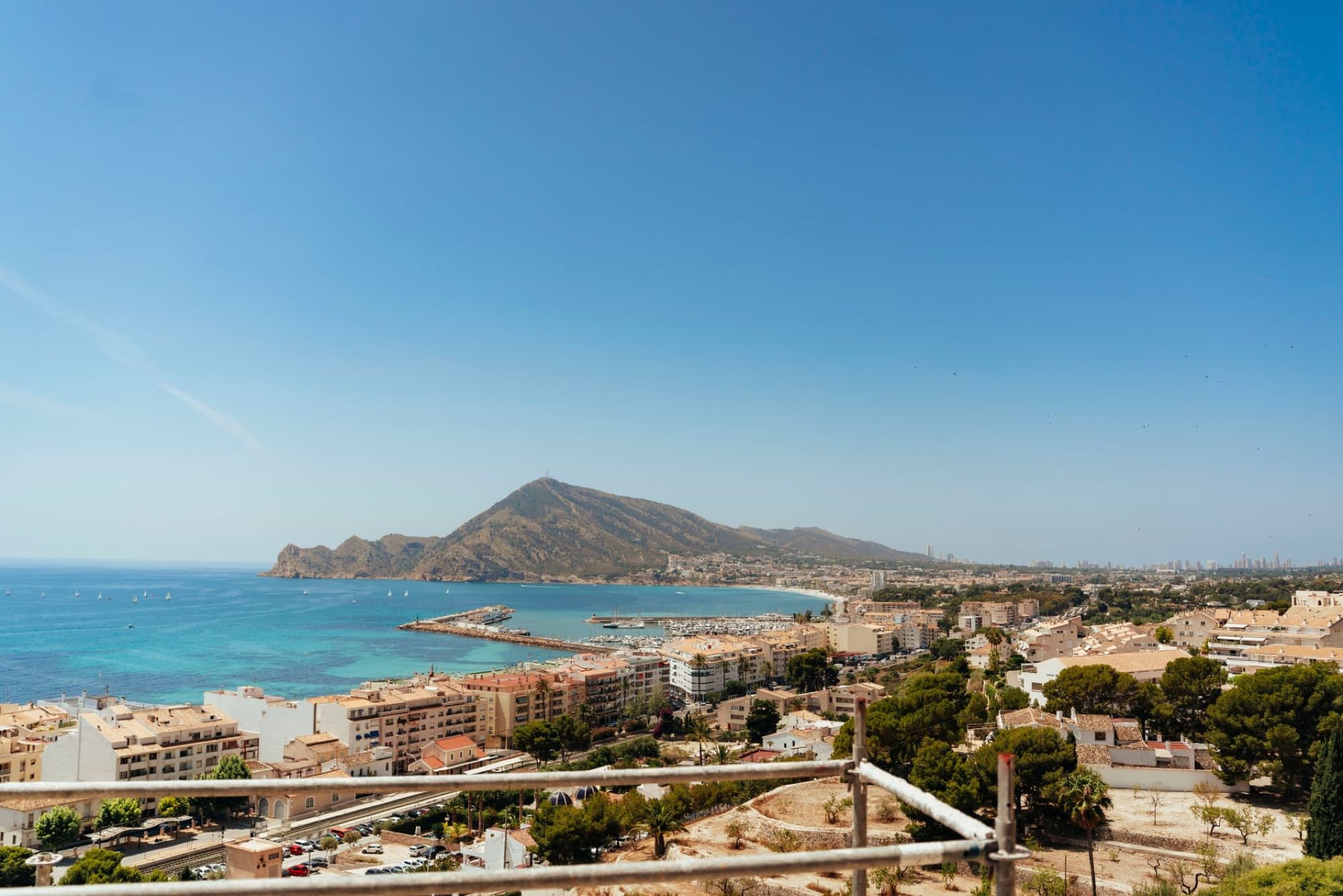 Aerial view of Altea's picturesque coastline, marina, and cityscape with blue skies and mountains.