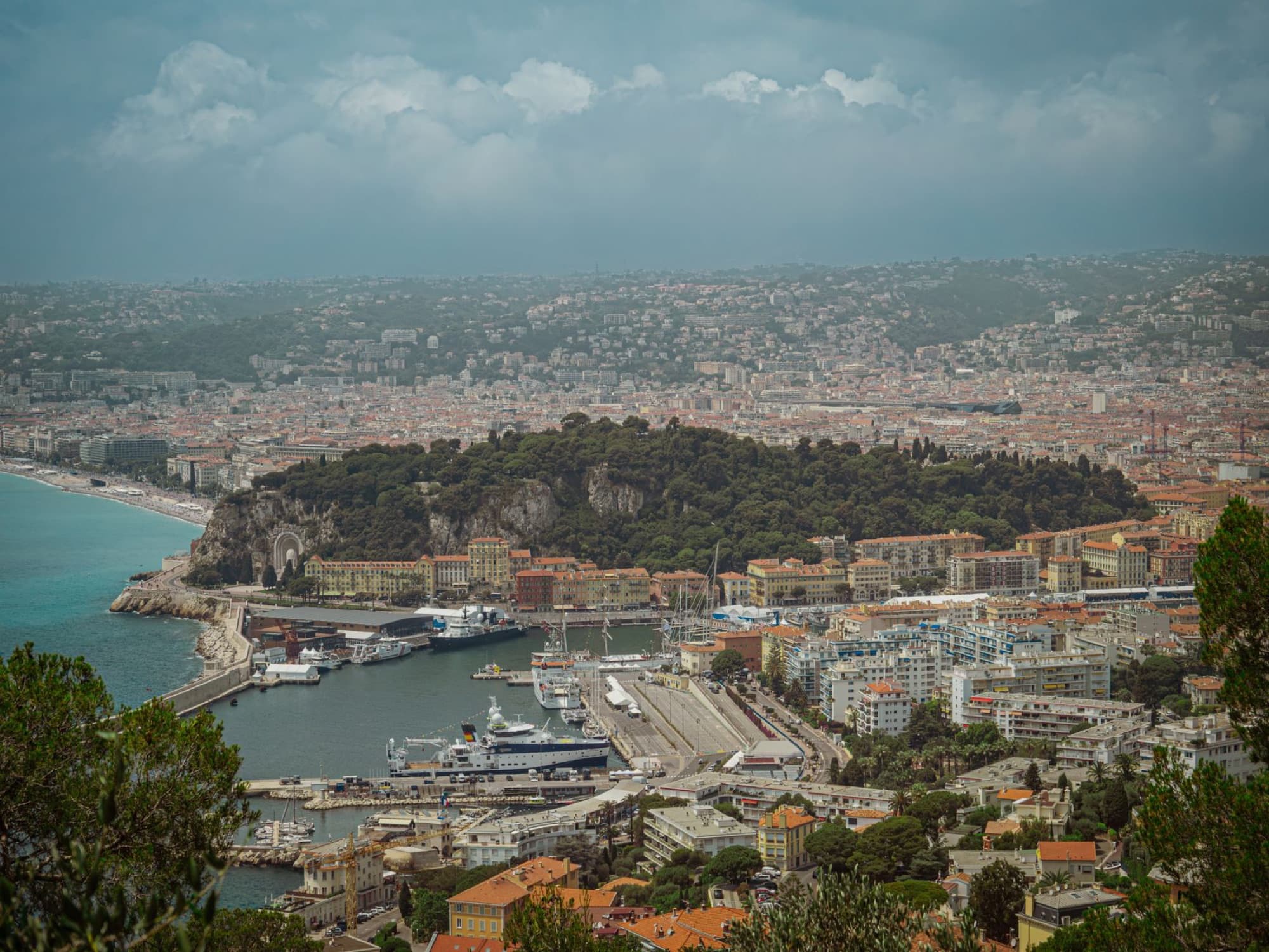 Stunning aerial view of Nice, France, showcasing the harbor, coastline, and urban landscape under a cloudy sky.
