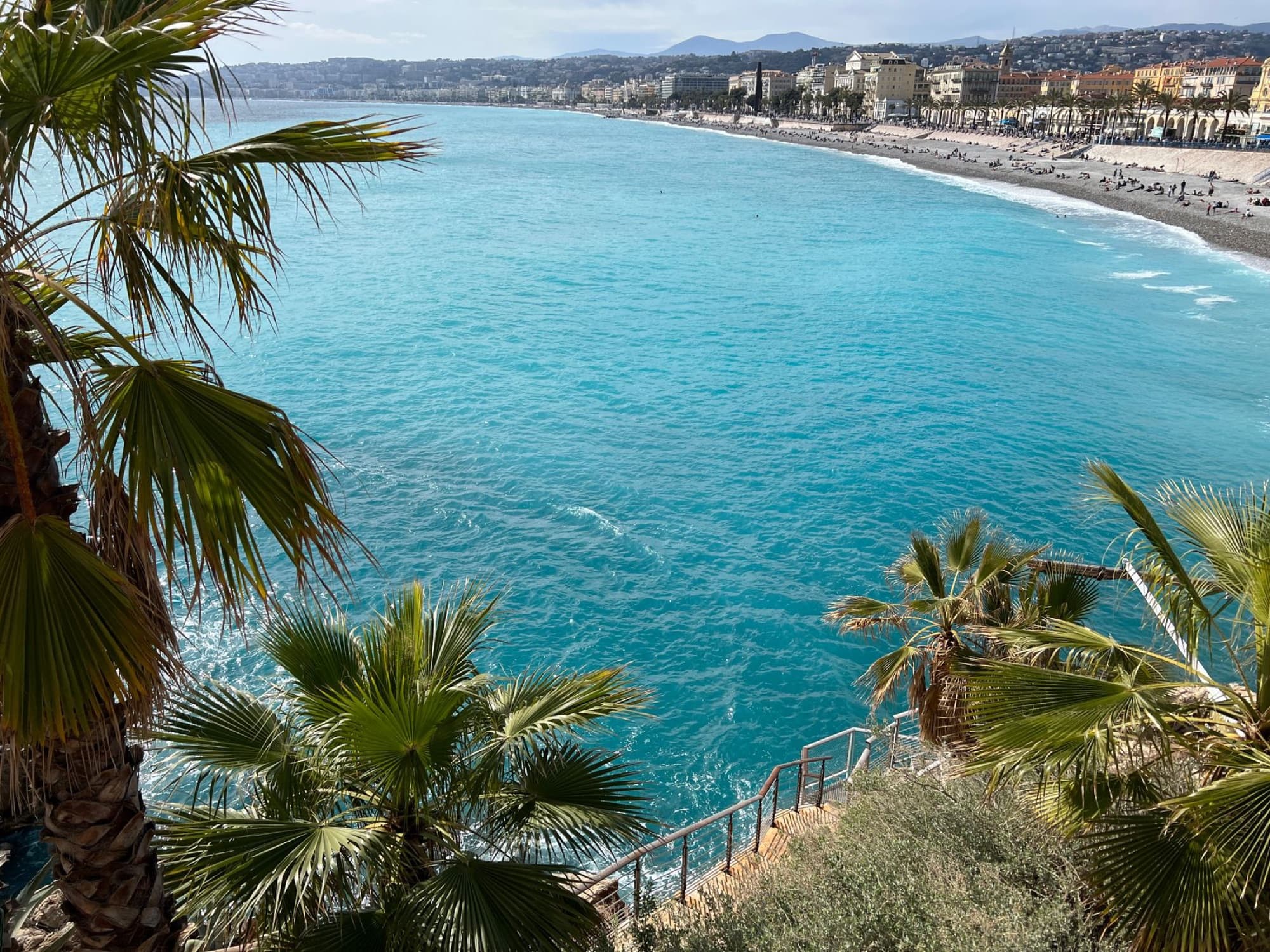Aerial view of the beautiful coastline and vibrant city of Nice, France, with palm trees and turquoise sea.