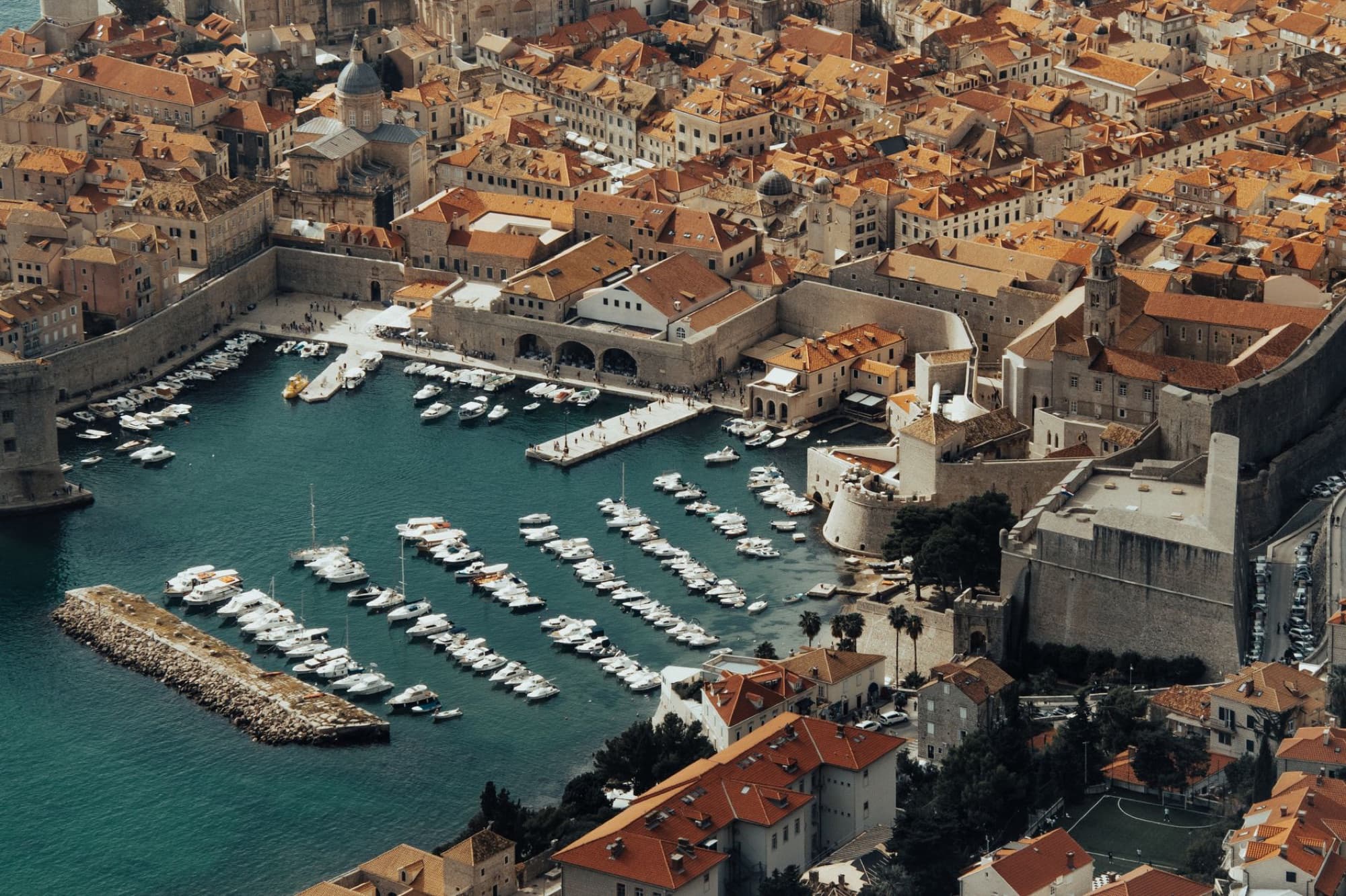 Stunning aerial view of Dubrovnik's ancient city walls and harbor filled with boats under the summer sun.