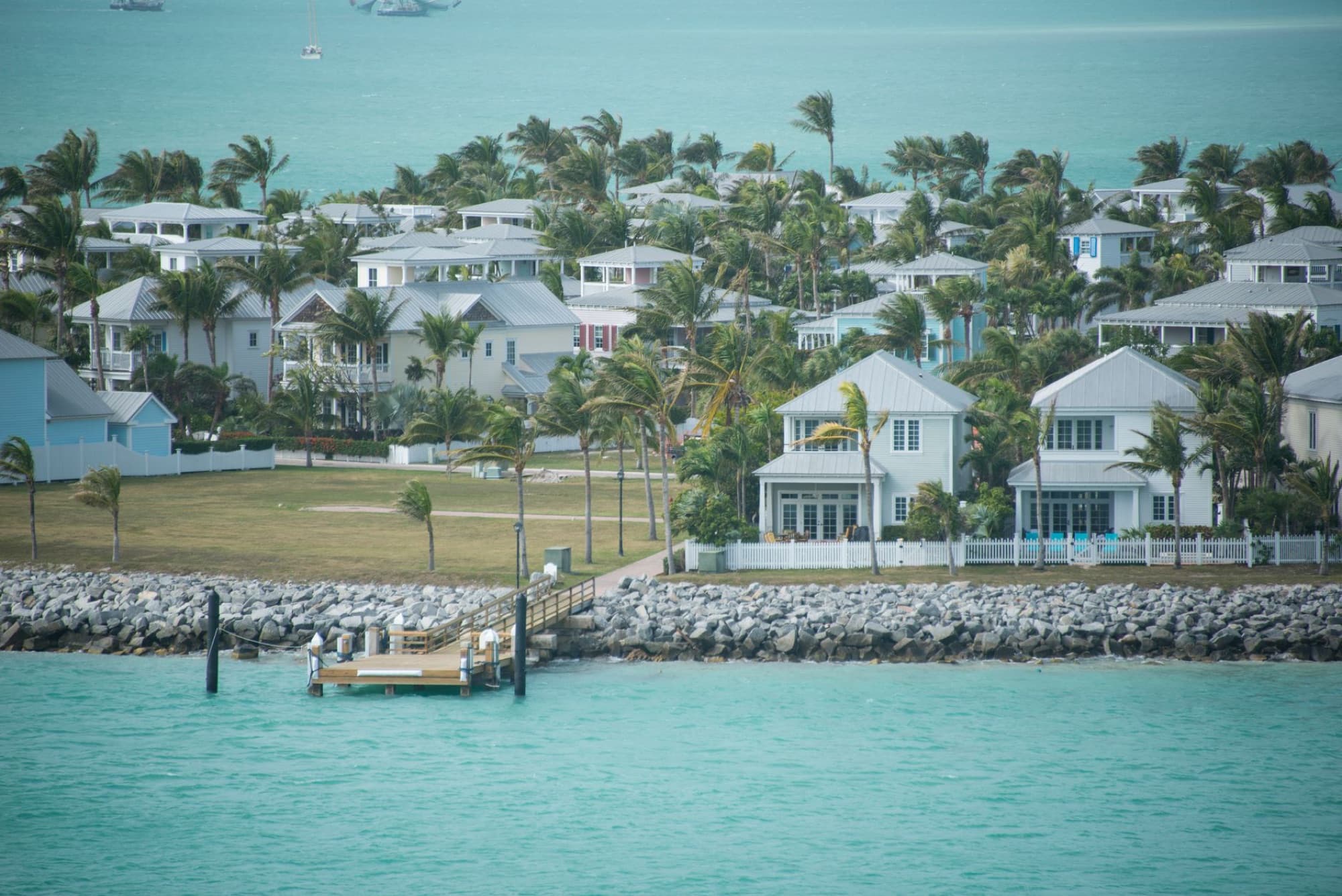 Aerial view of luxury coastal residences with palm trees by turquoise waters.
