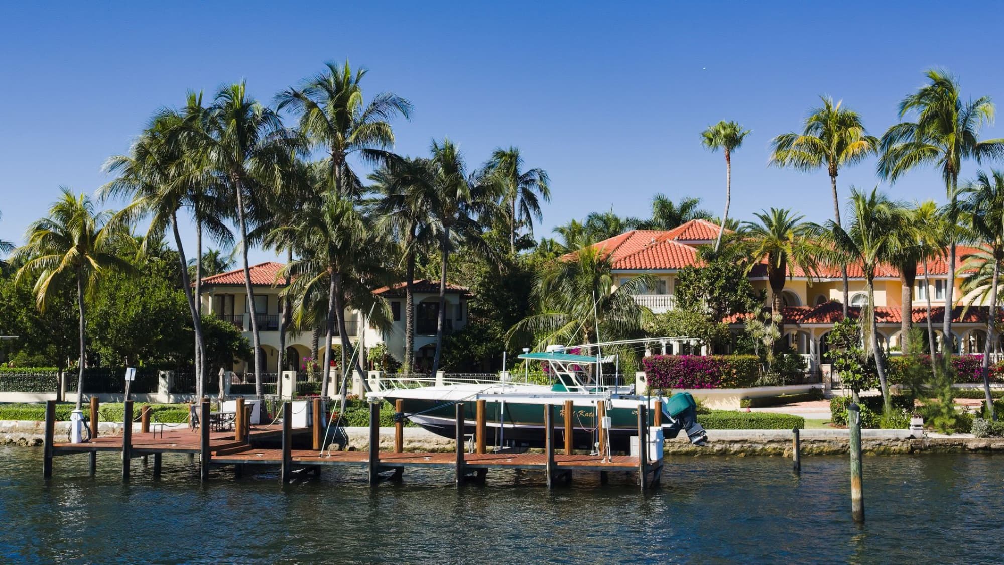 Scenic view of luxury waterfront homes with palm trees and a boat docked in Fort Lauderdale, Florida.