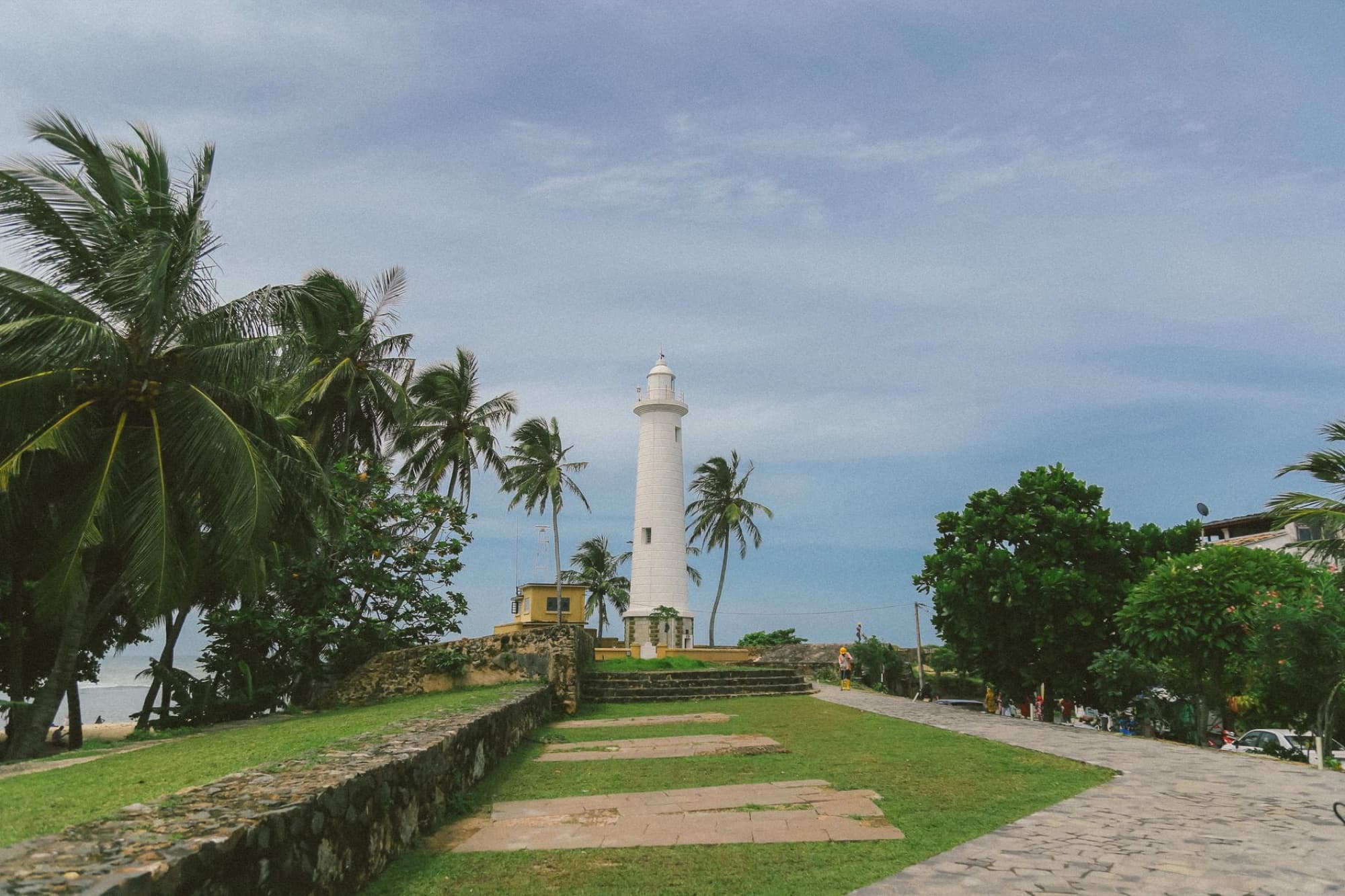 Scenic view of Galle Lighthouse surrounded by tropical palm trees and blue sky in Sri Lanka.