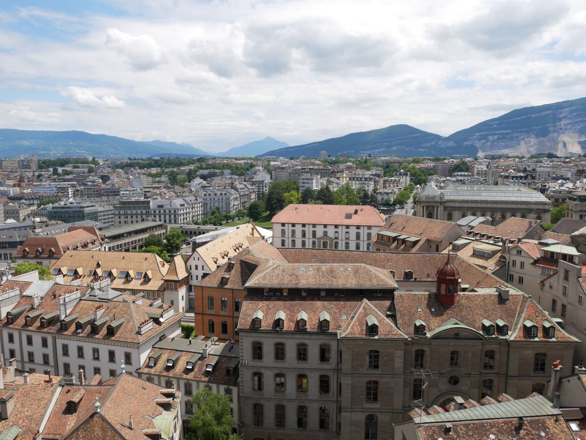 Aerial view of picturesque old town rooftops with mountain backdrop on a sunny day.