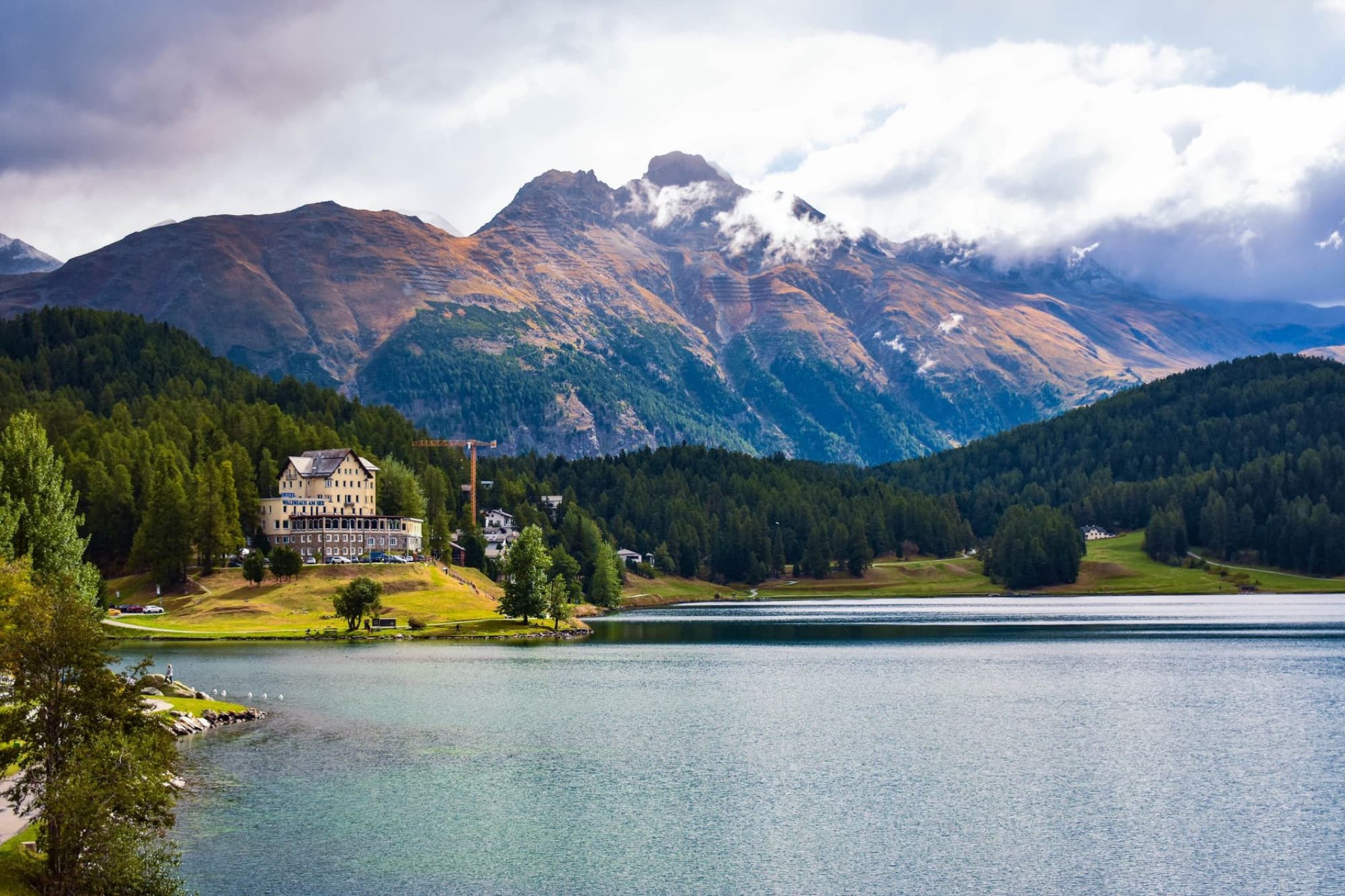 Scenic view of San Maurizio Lake with mountains and forest in Switzerland's Graubünden region.