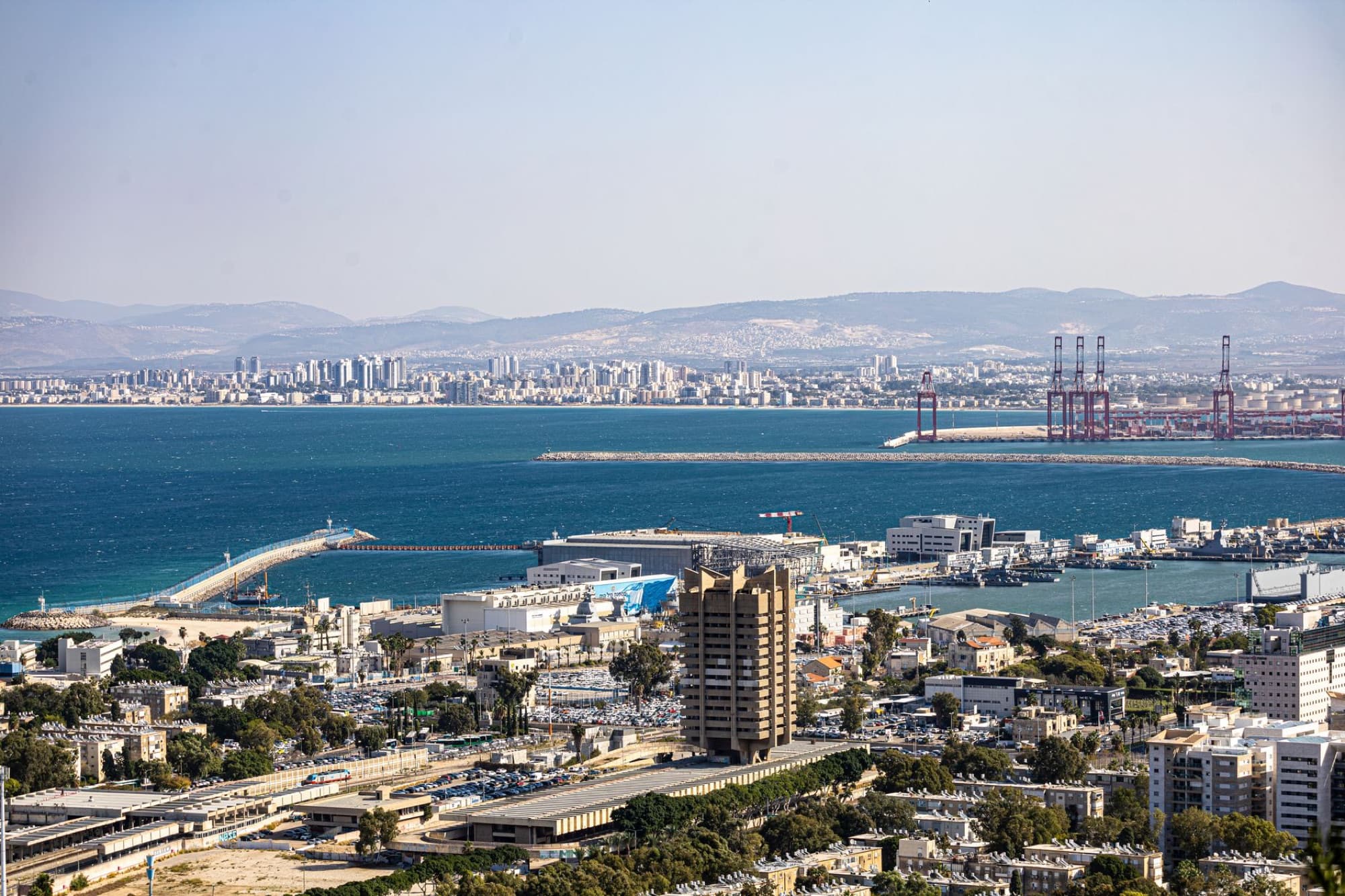 Vibrant aerial view of Haifa port with cityscape and mountains in the background under clear skies.
