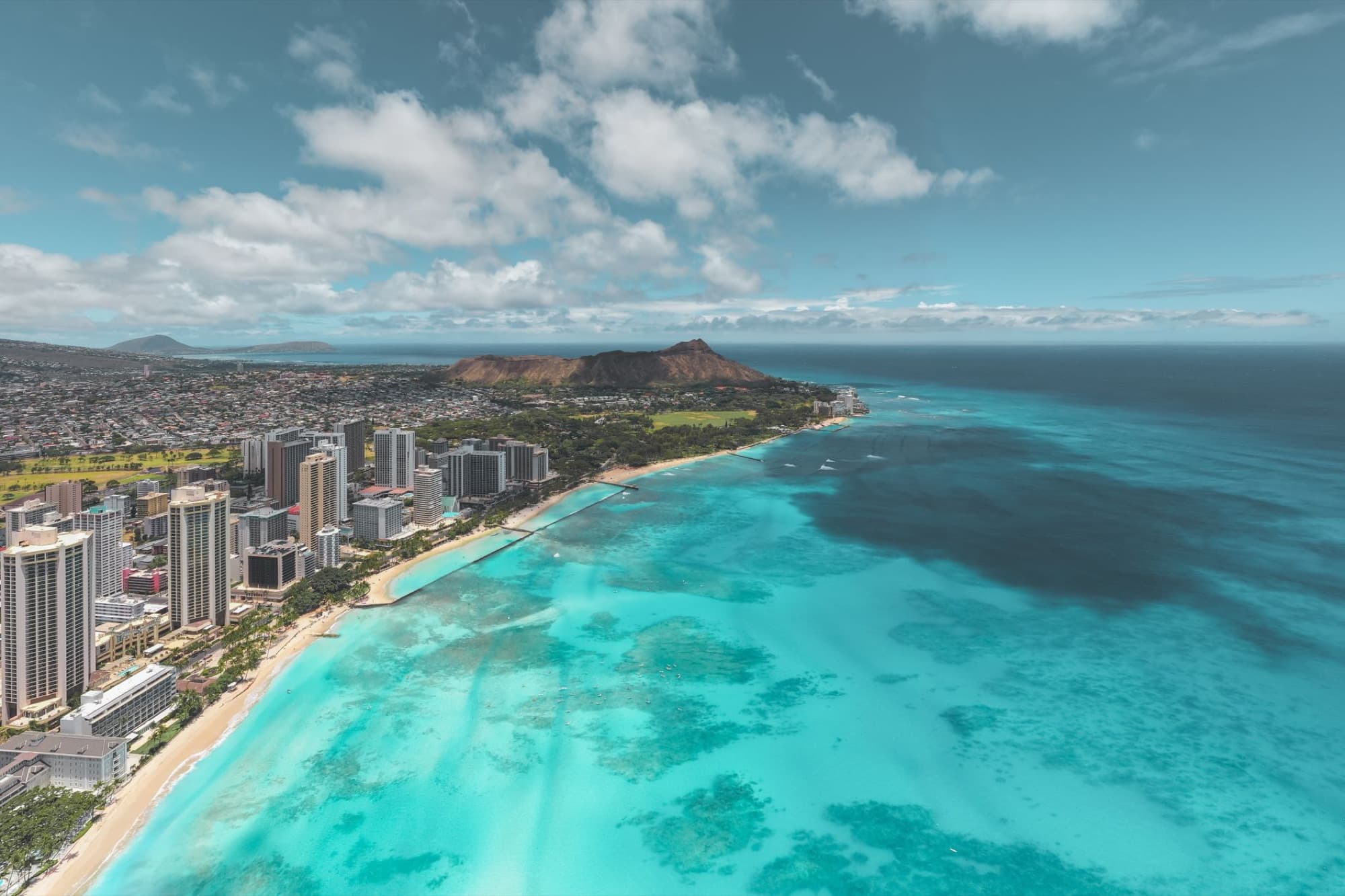 Stunning aerial shot of Waikiki Beach with the iconic Diamond Head in the background, showcasing Honolulu's skyline against the turquoise ocean.