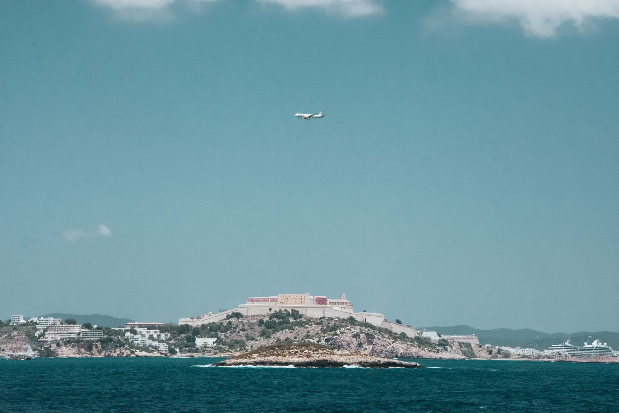 Scenic view of Ibiza's coastline with an airplane flying over the Mediterranean Sea.