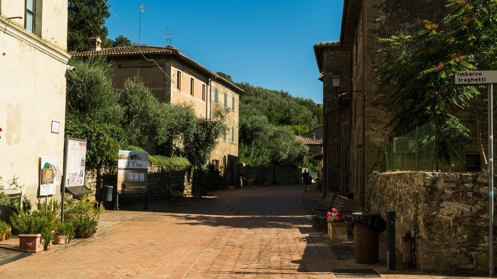 Scenic small town street in Umbria, Italy with rustic architecture and lush greenery under a bright blue sky.
