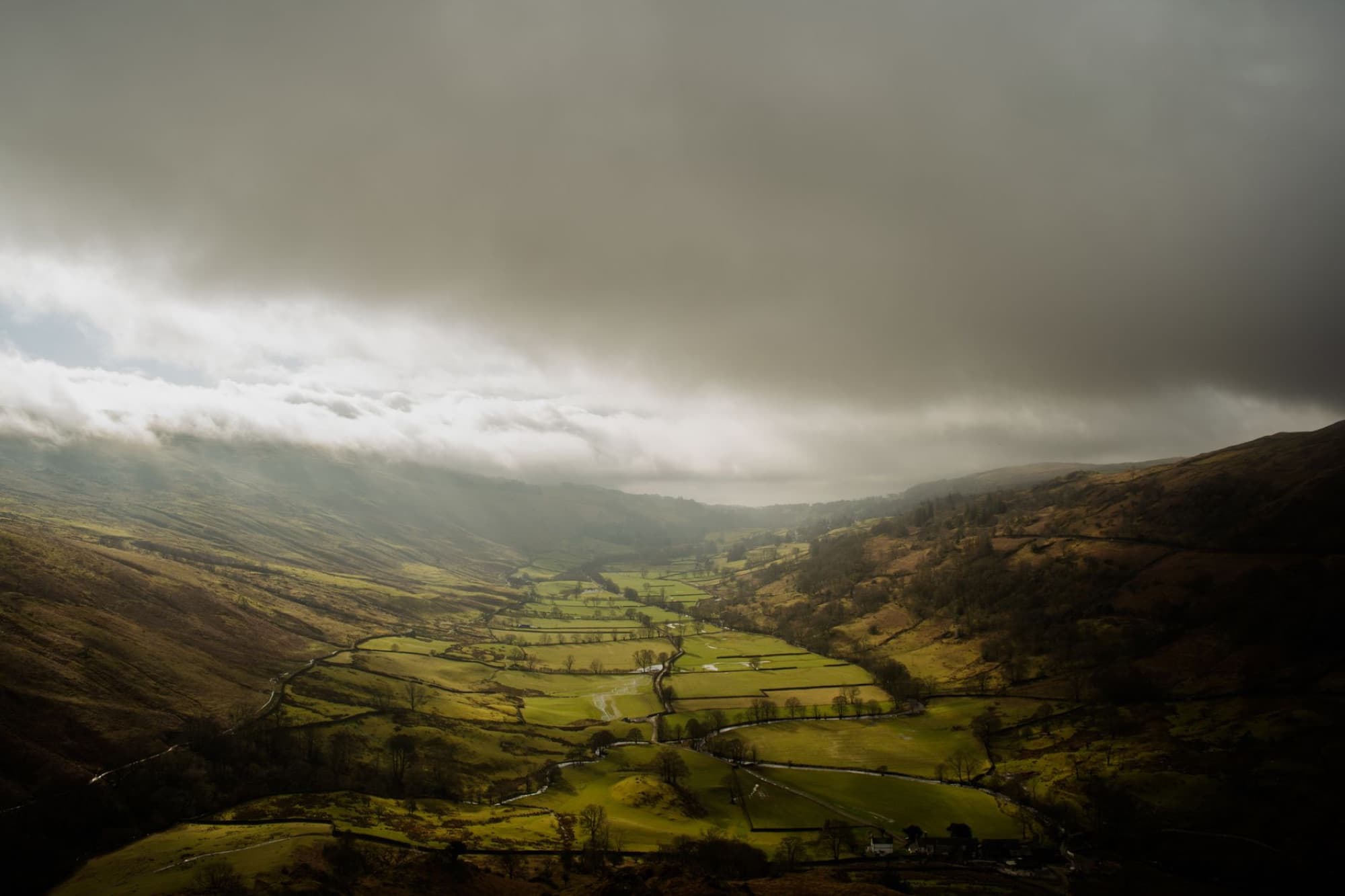 Scenic aerial of lush valleys under dramatic skies in England's Lake District.