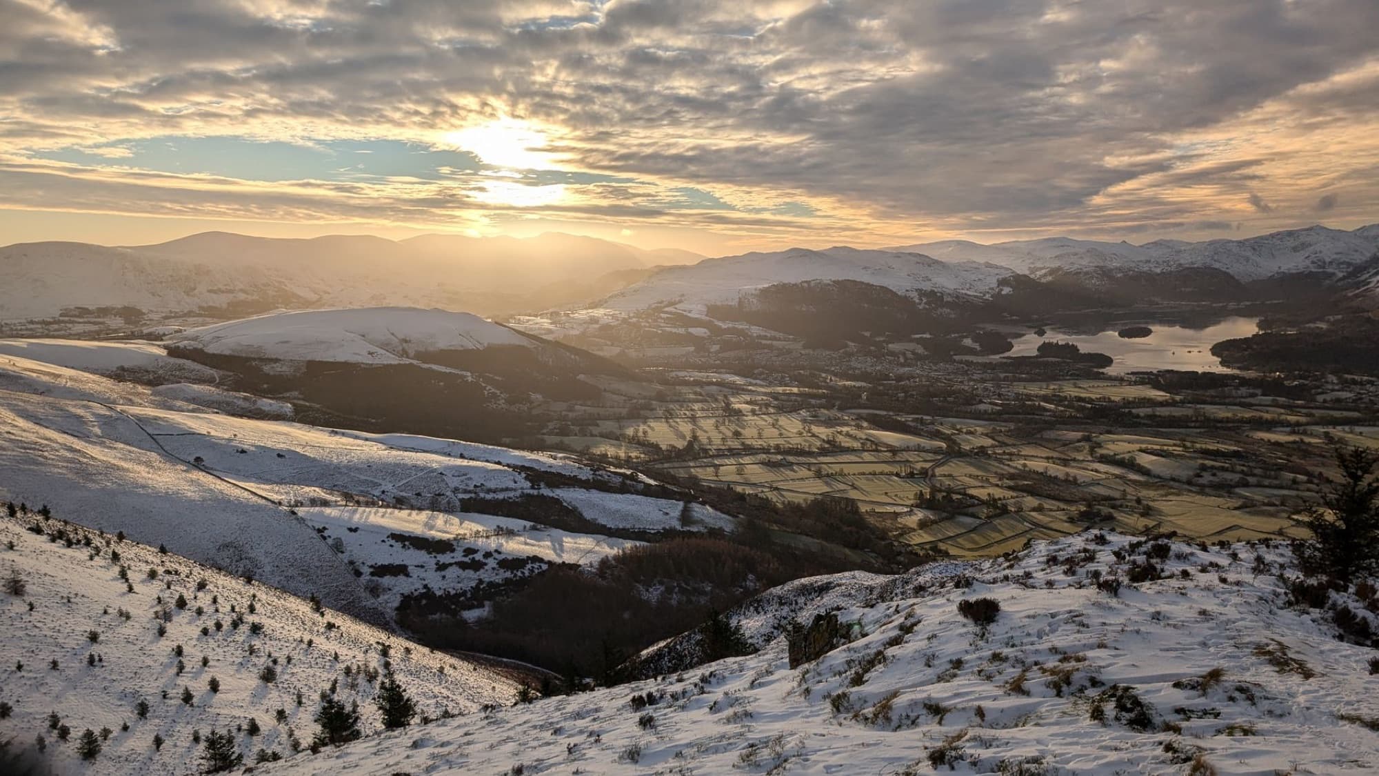 Capture the serene beauty of a snowy sunrise over the Lake District's majestic mountains.
