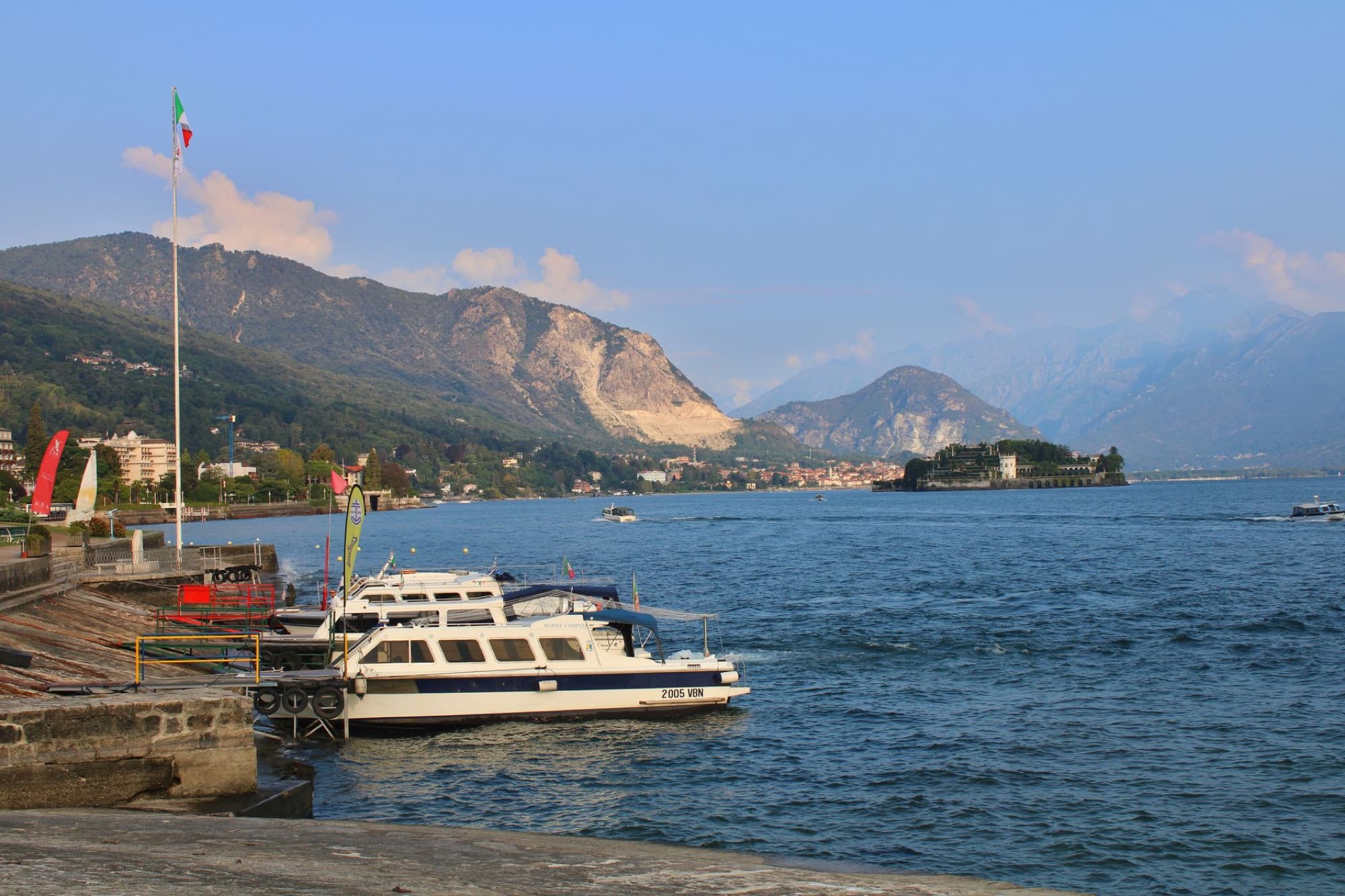 Beautiful view of Lake Maggiore with boats docked, scenic mountains, and coastline in Stresa, Italy.
