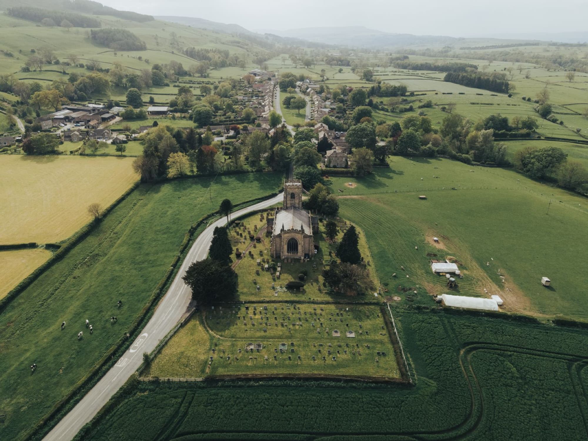 Drone shot of a church surrounded by green fields and countryside village in tranquil rural setting.