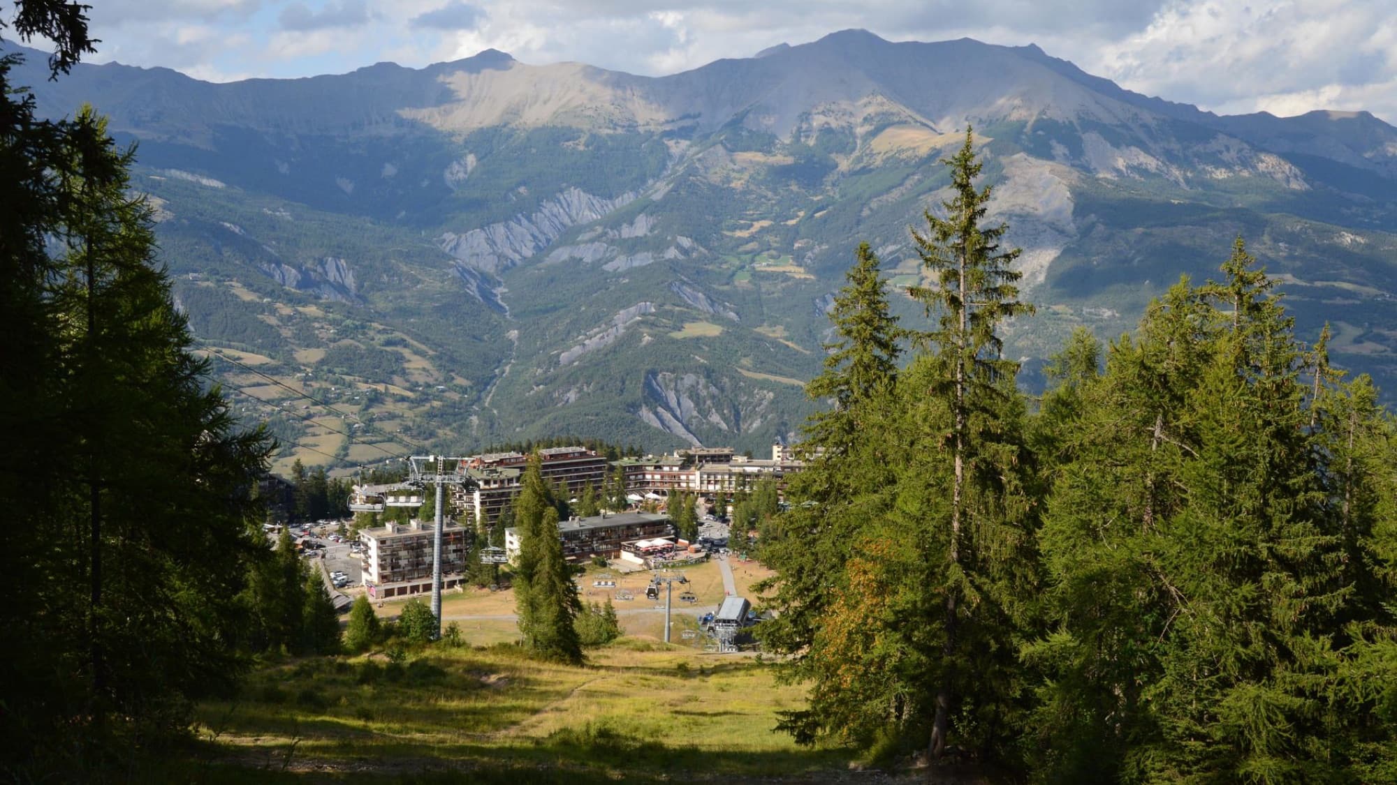 A scenic view of a mountain resort surrounded by lush green trees and expansive peaks.