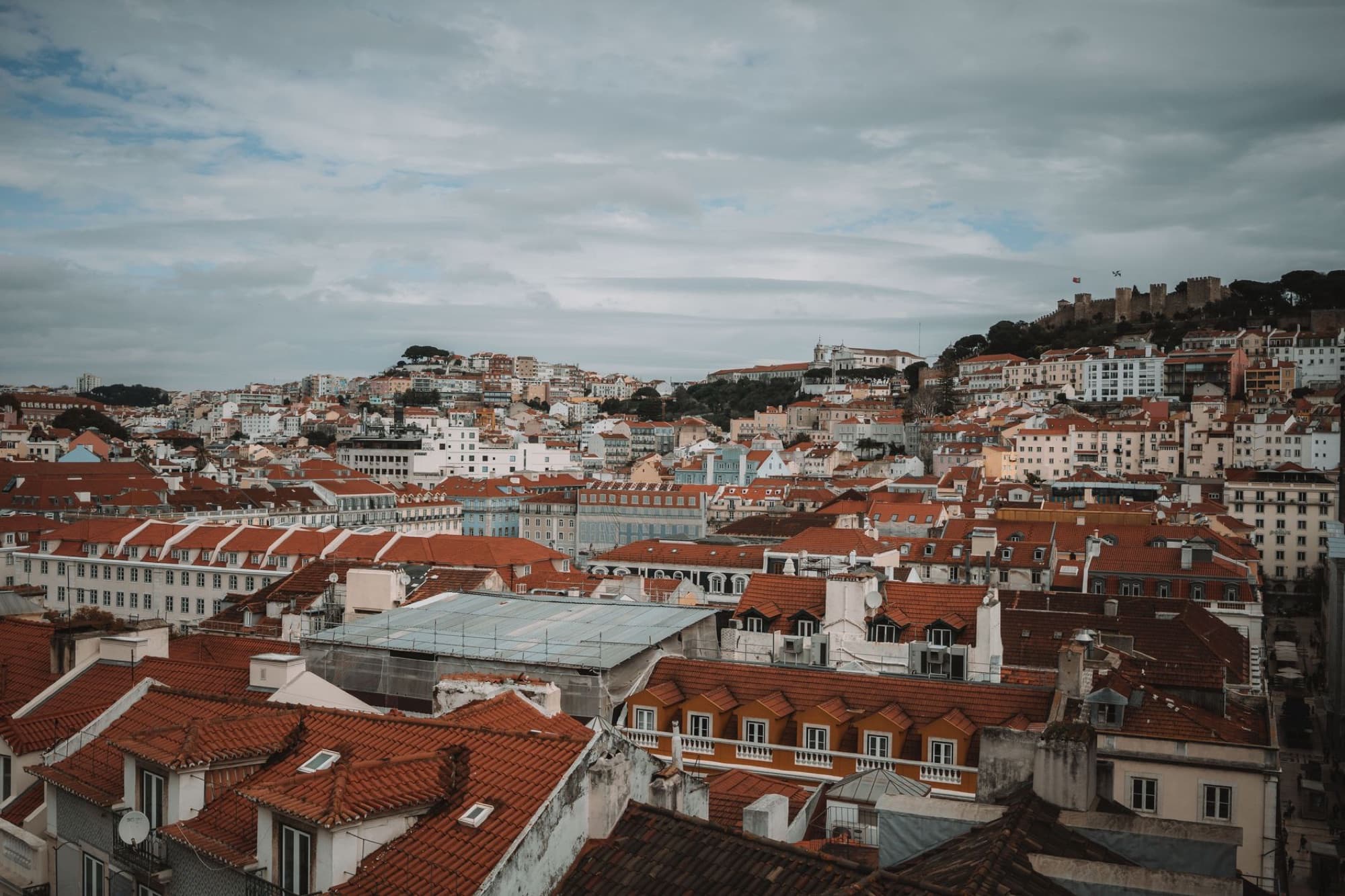 A scenic view of Lisbon's red rooftops and historic castle under a cloudy sky.