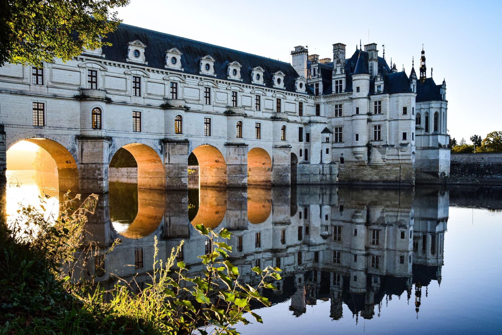 Elegant reflection of Château de Chenonceau on the Cher River at sunrise in the Loire Valley.