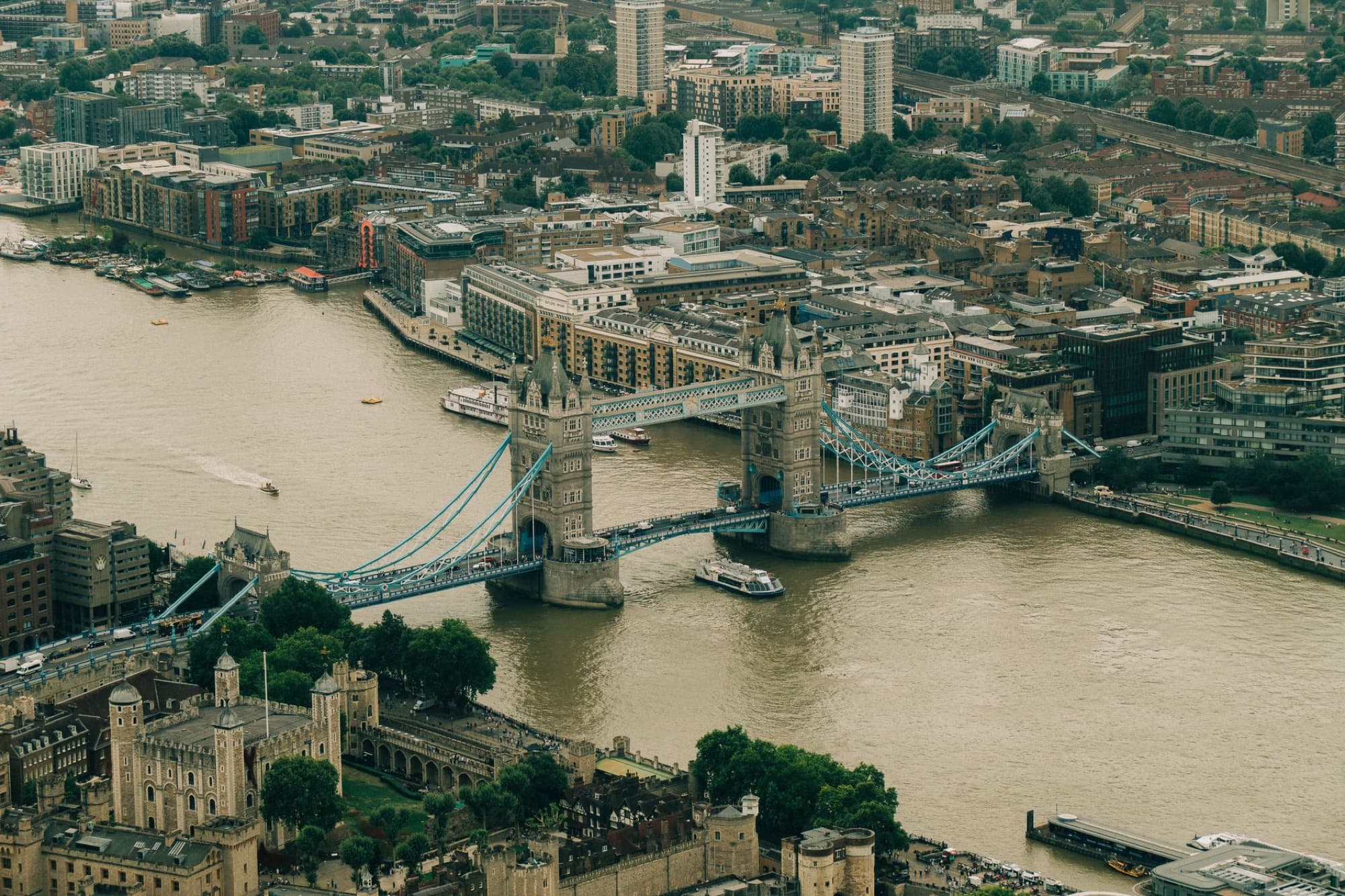 Aerial view showcasing the Tower Bridge over the Thames River in London, UK amidst urban landscape.