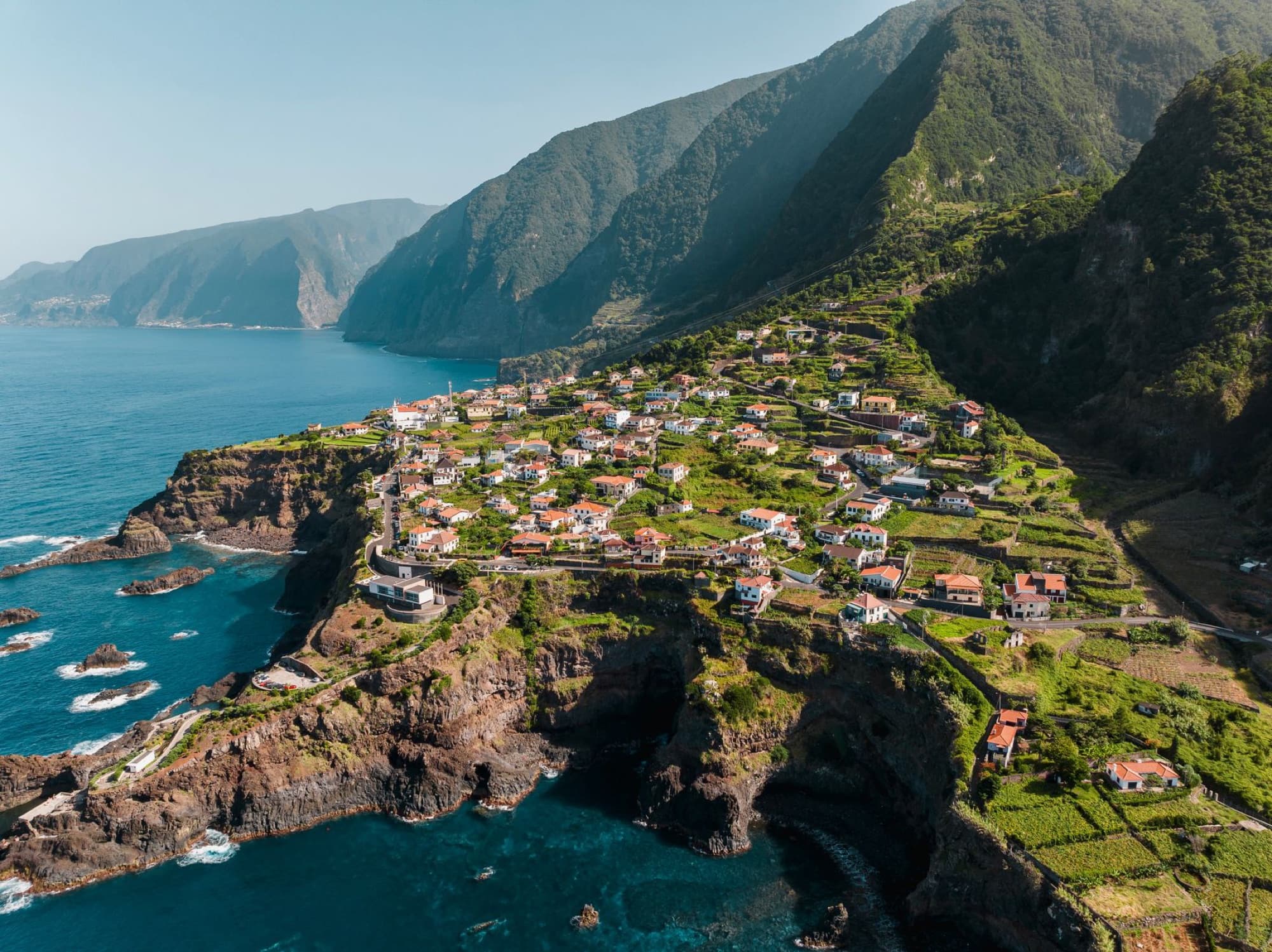 Scenic aerial shot of a coastal village in Funchal, Madeira, surrounded by cliffs and ocean.