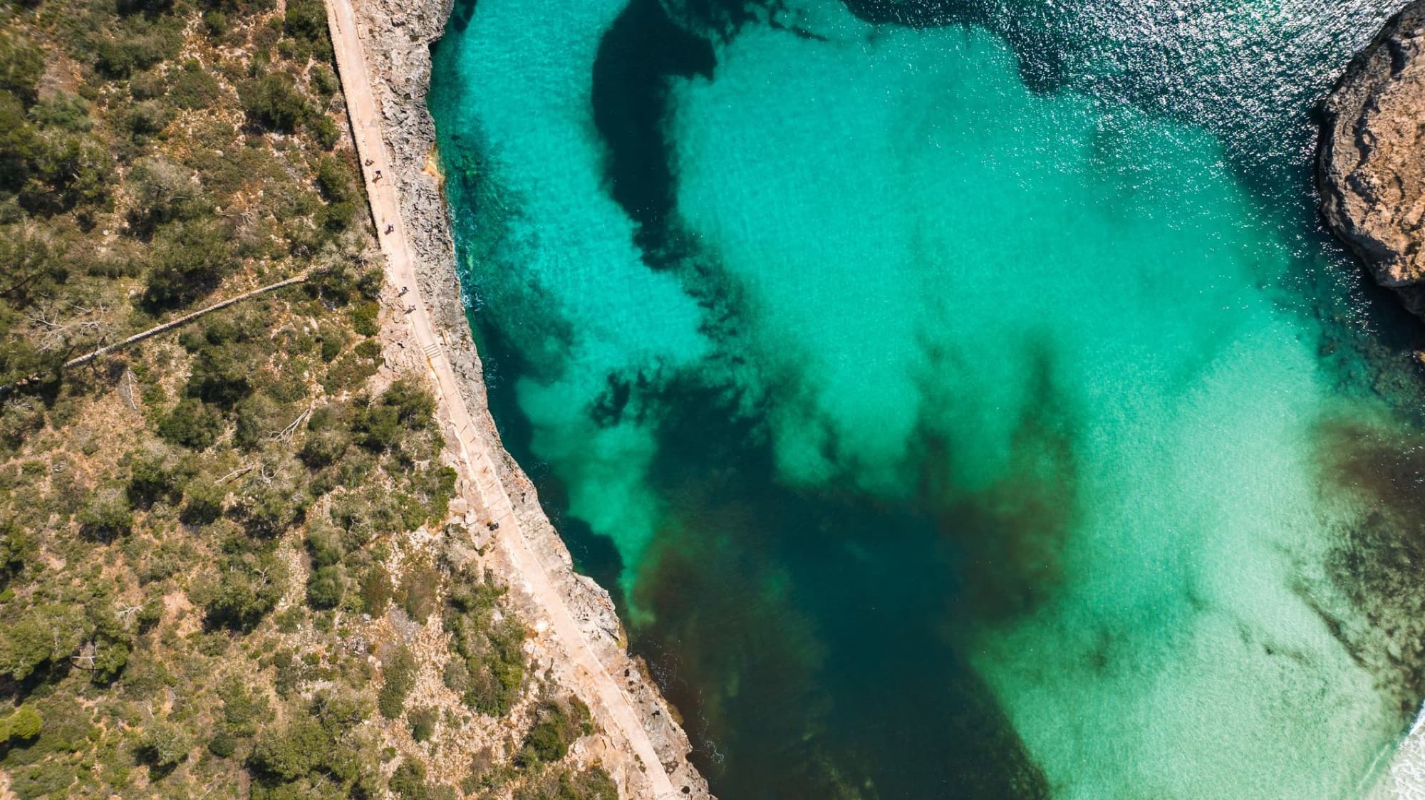 Aerial shot of Mallorca's pristine turquoise bay with rocky cliffs and vivid waters under the summer sun.