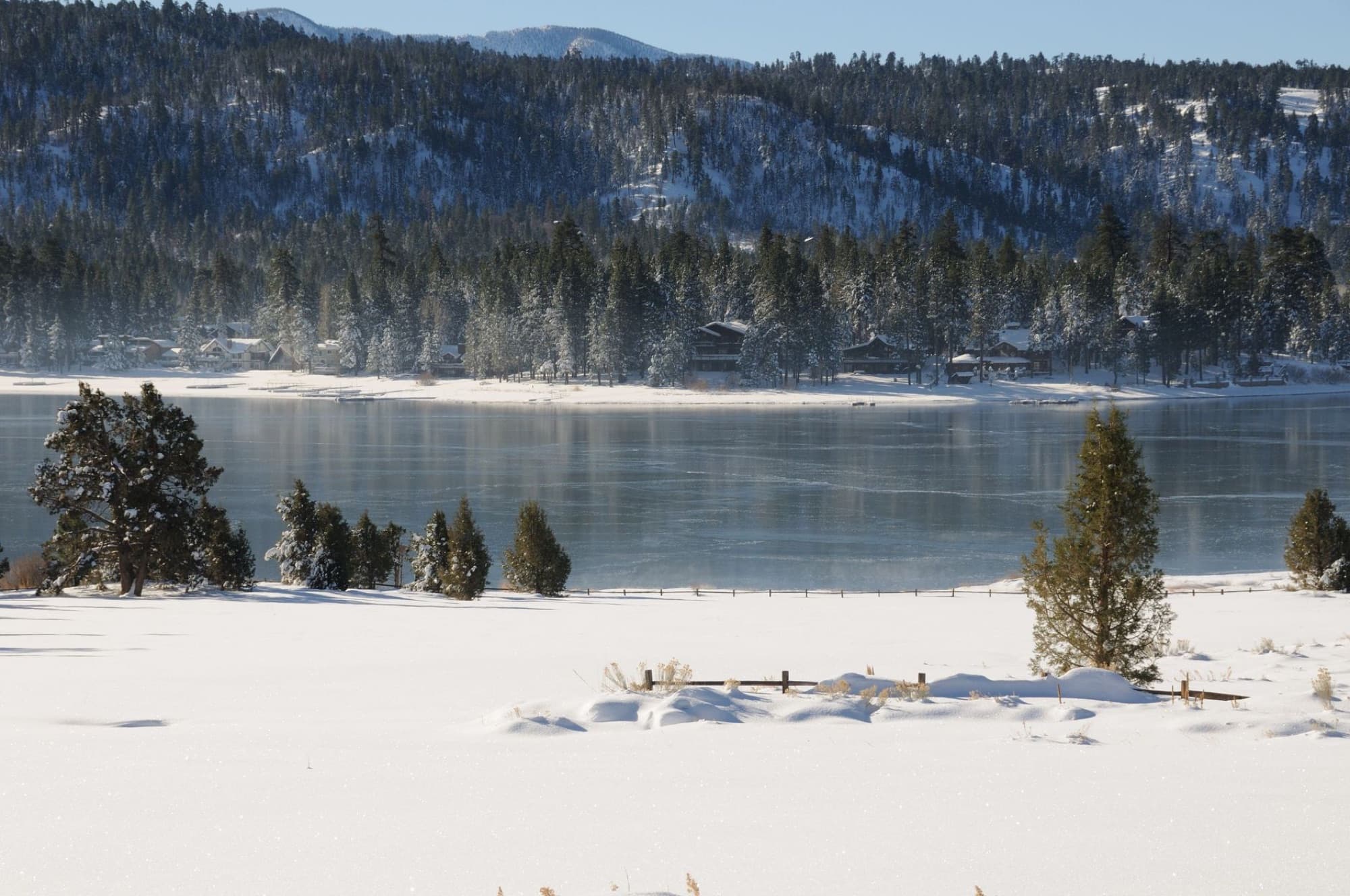 Scenic view of a snow-covered lake surrounded by snowy trees and mountains on a clear winter day.