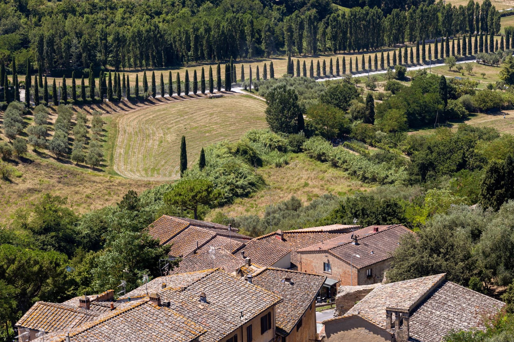 A picturesque aerial shot of a Tuscan village surrounded by lush greenery and cypress trees.