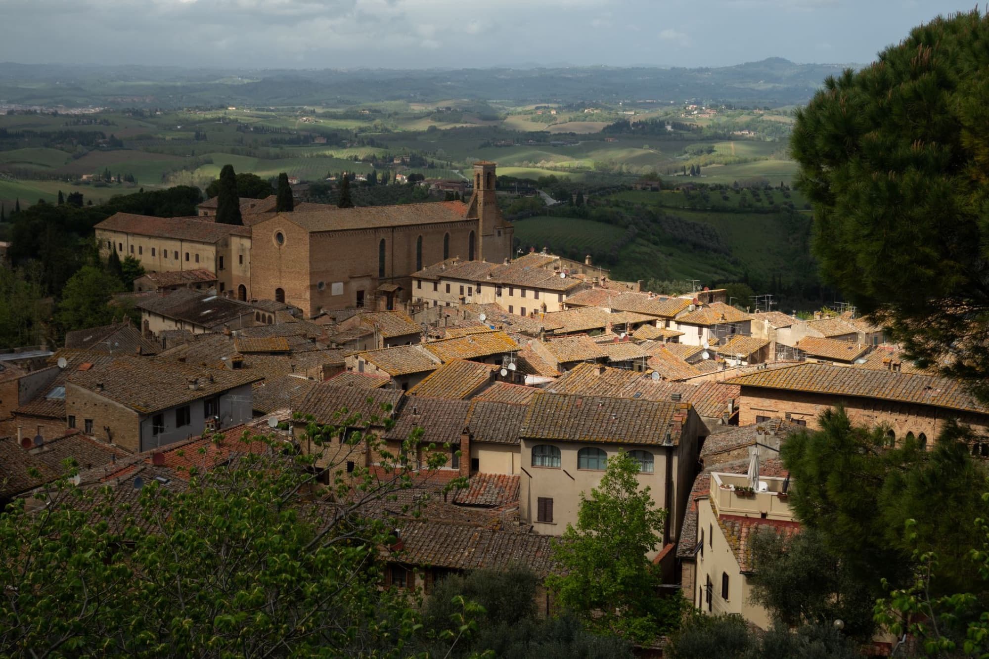 Aerial view of historical Tuscan rooftops and countryside, capturing serene rolling hills and rustic architecture.