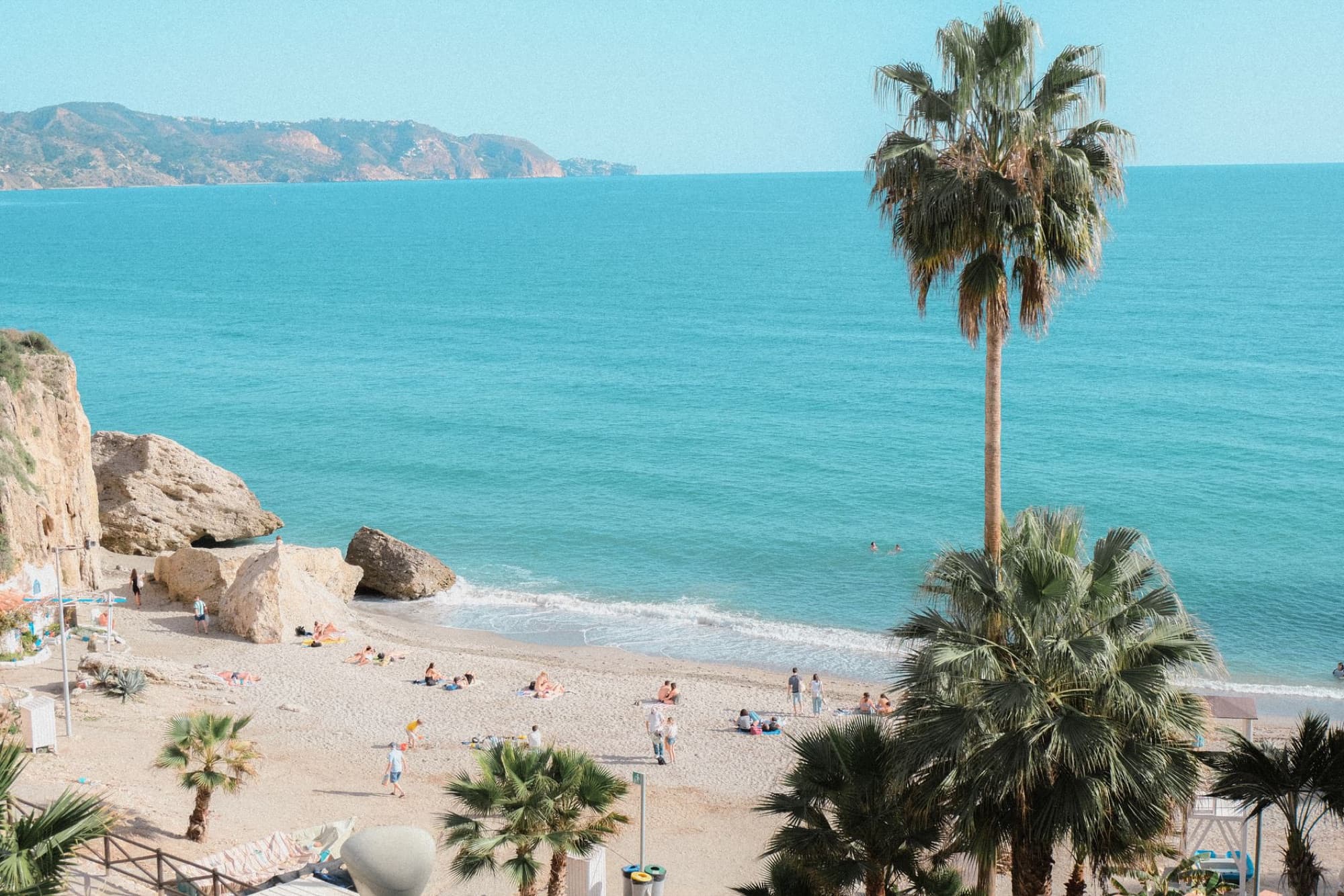 Beautiful beach scene in Nerja, Andalusia, Spain featuring palm trees and clear blue sea.