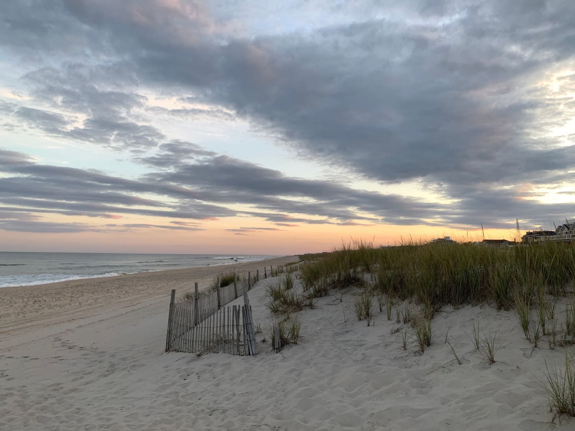 Scenic sunset view over beach dunes in New Jersey with vibrant sky and ocean waves.