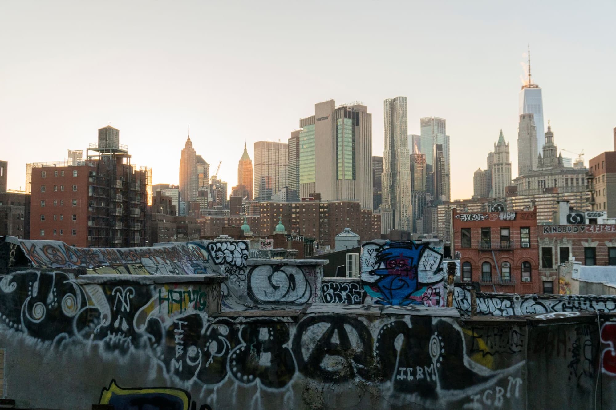 View of New York City skyline from a graffiti-covered rooftop at sunset.