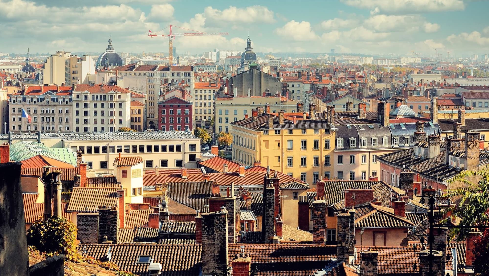 Aerial view of Lyon's historic rooftops and skyline under a bright blue sky.