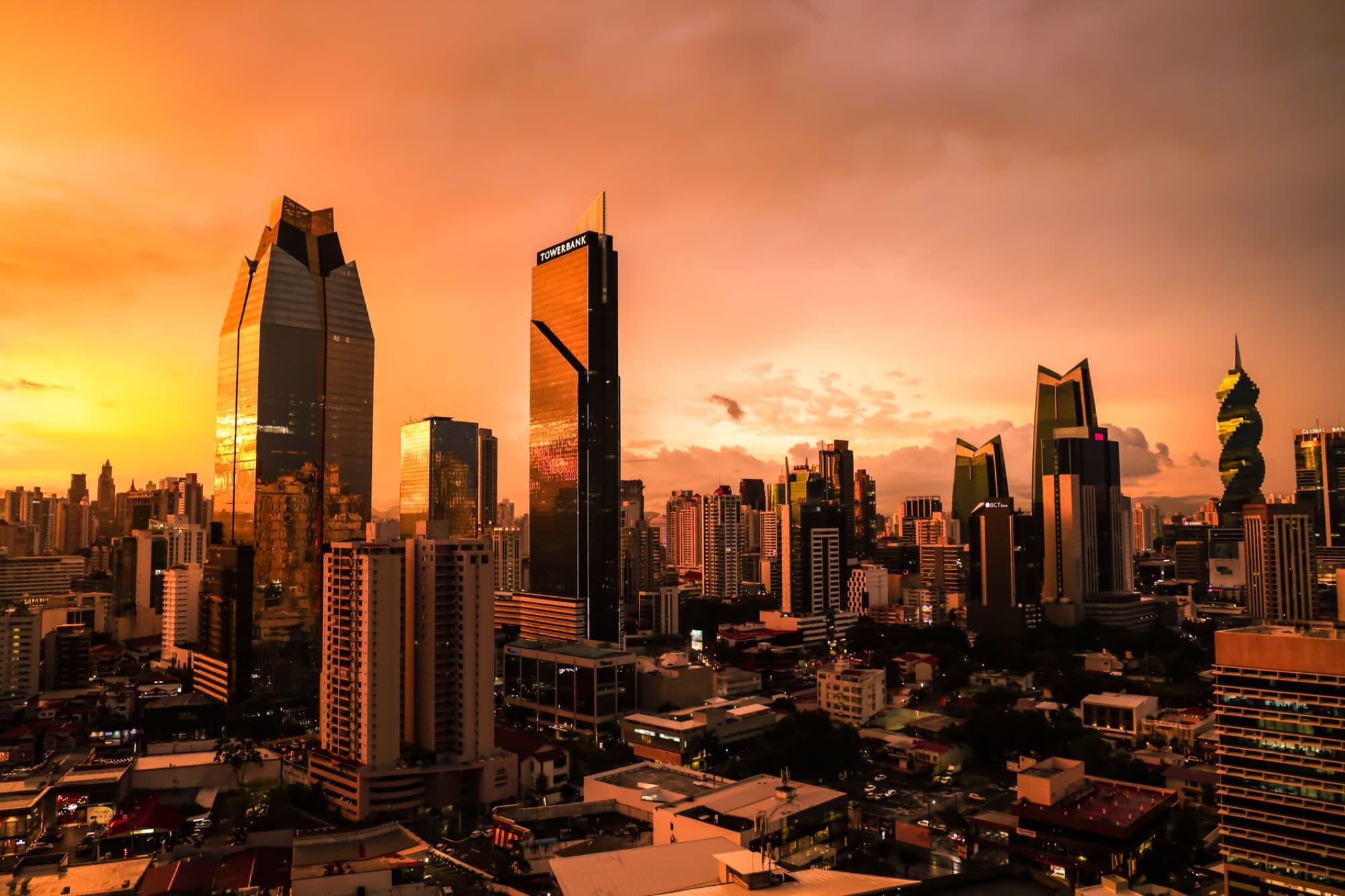 The sun sets over Panama City's skyline, casting a warm glow on skyscrapers and urban landscape.