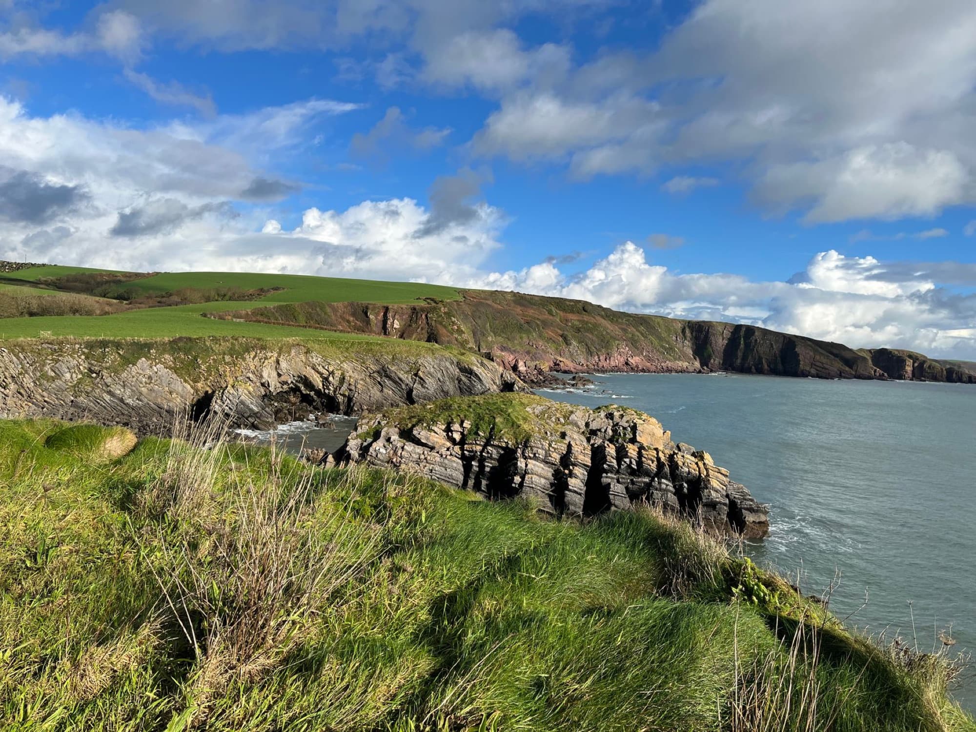 Breathtaking view of the coastal cliffs and grassy landscape in Pembrokeshire, UK under a bright sky.