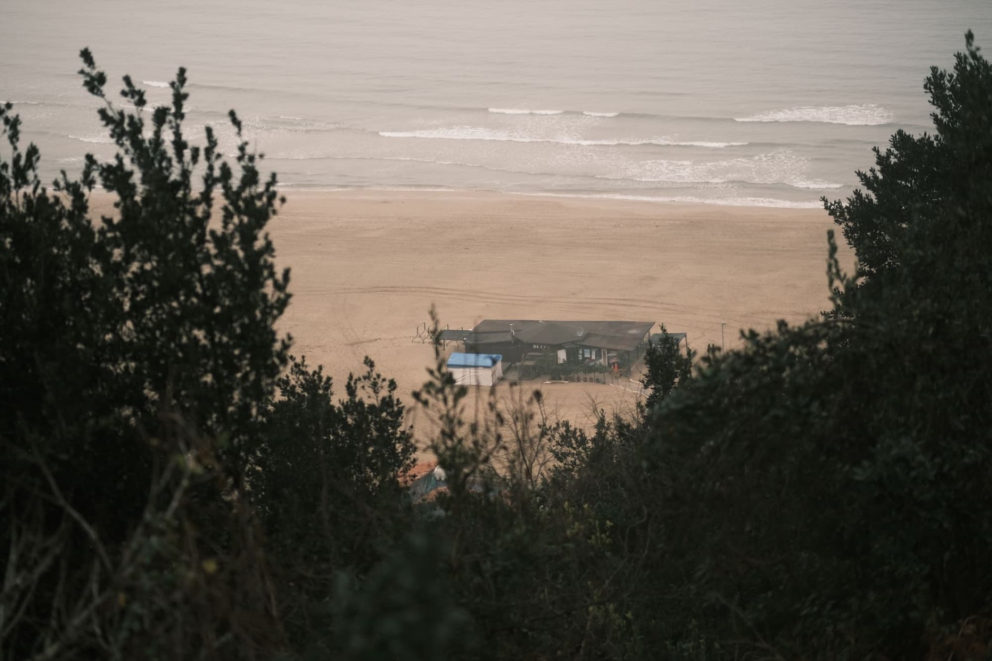 A serene aerial view of a coastal beach house surrounded by waves and trees.