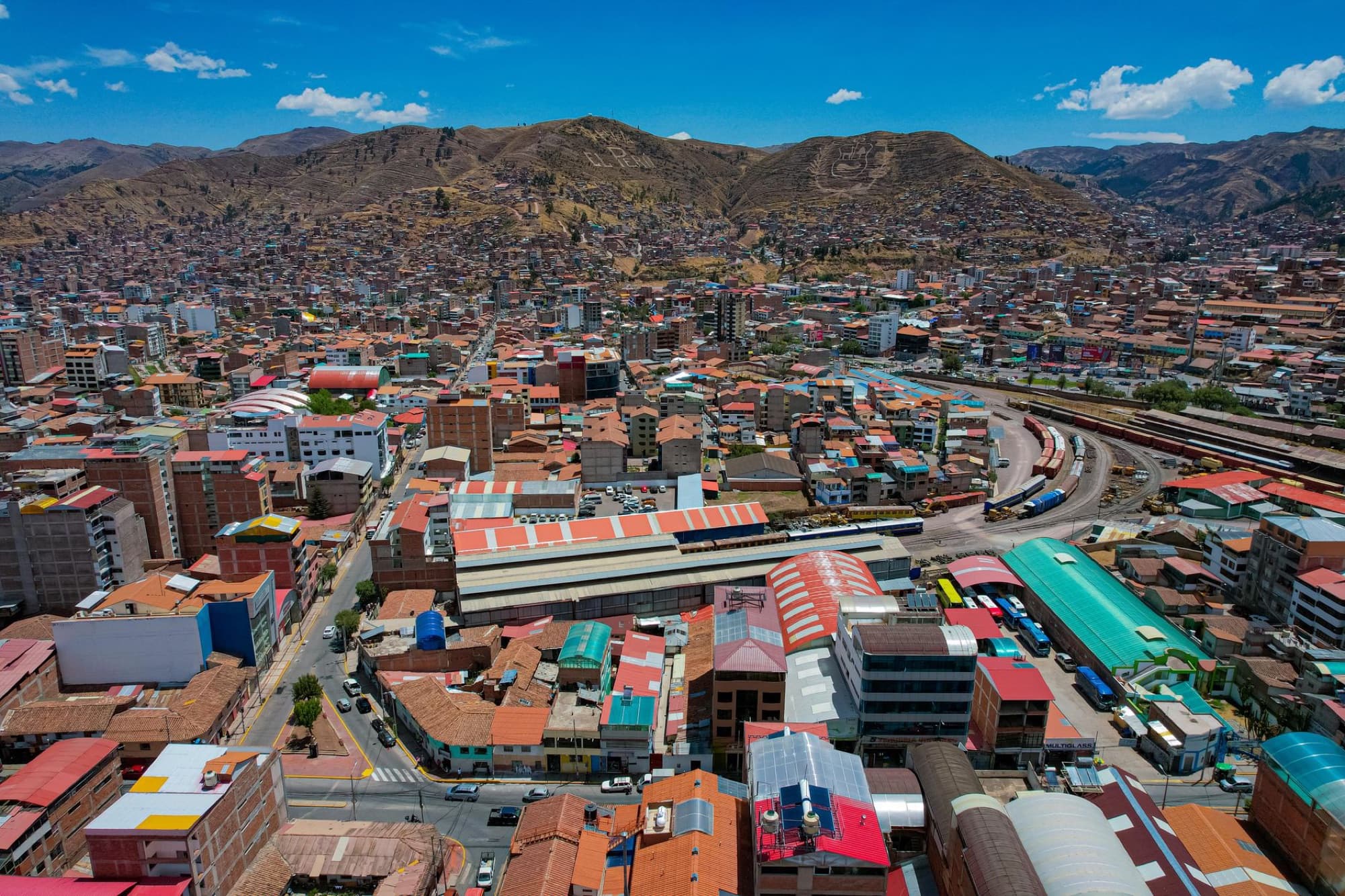 Aerial view of Cusco, Peru, showcasing the colorful rooftops and surrounding mountains under a clear blue sky.