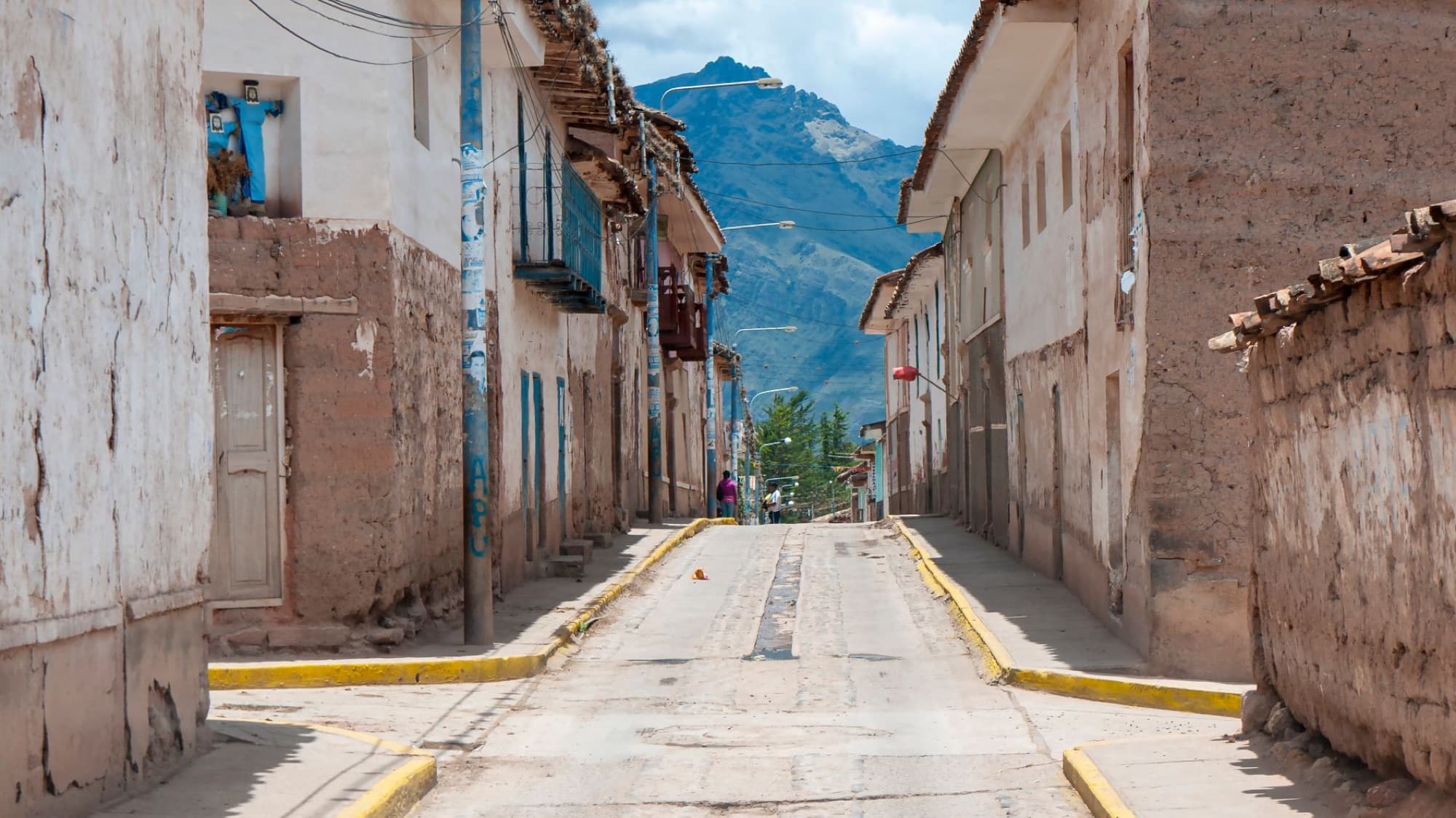 Discover the rustic charm of a narrow street in a traditional Peruvian town surrounded by stunning mountains.
