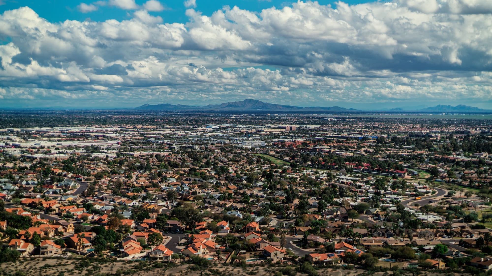 Aerial view of suburban rooftops under a cloudy sky with distant mountains in the background.