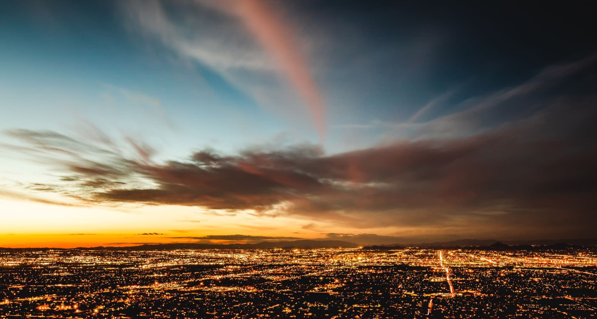 A breathtaking aerial view of a cityscape during sunset, showcasing vibrant colors and illuminated buildings.