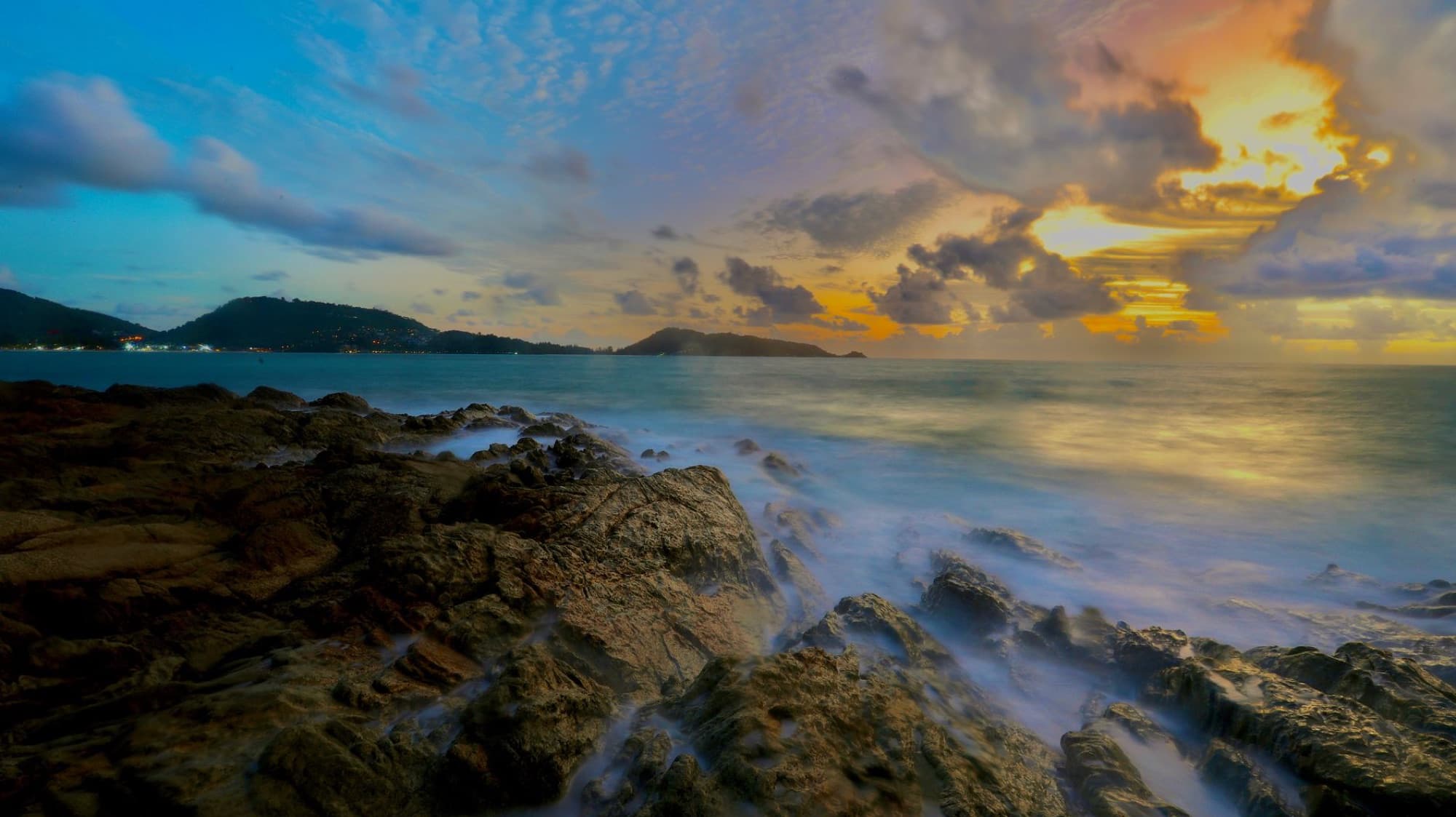 Serene view of sunset over rocky coastline at Patong Beach, Phuket, Thailand.