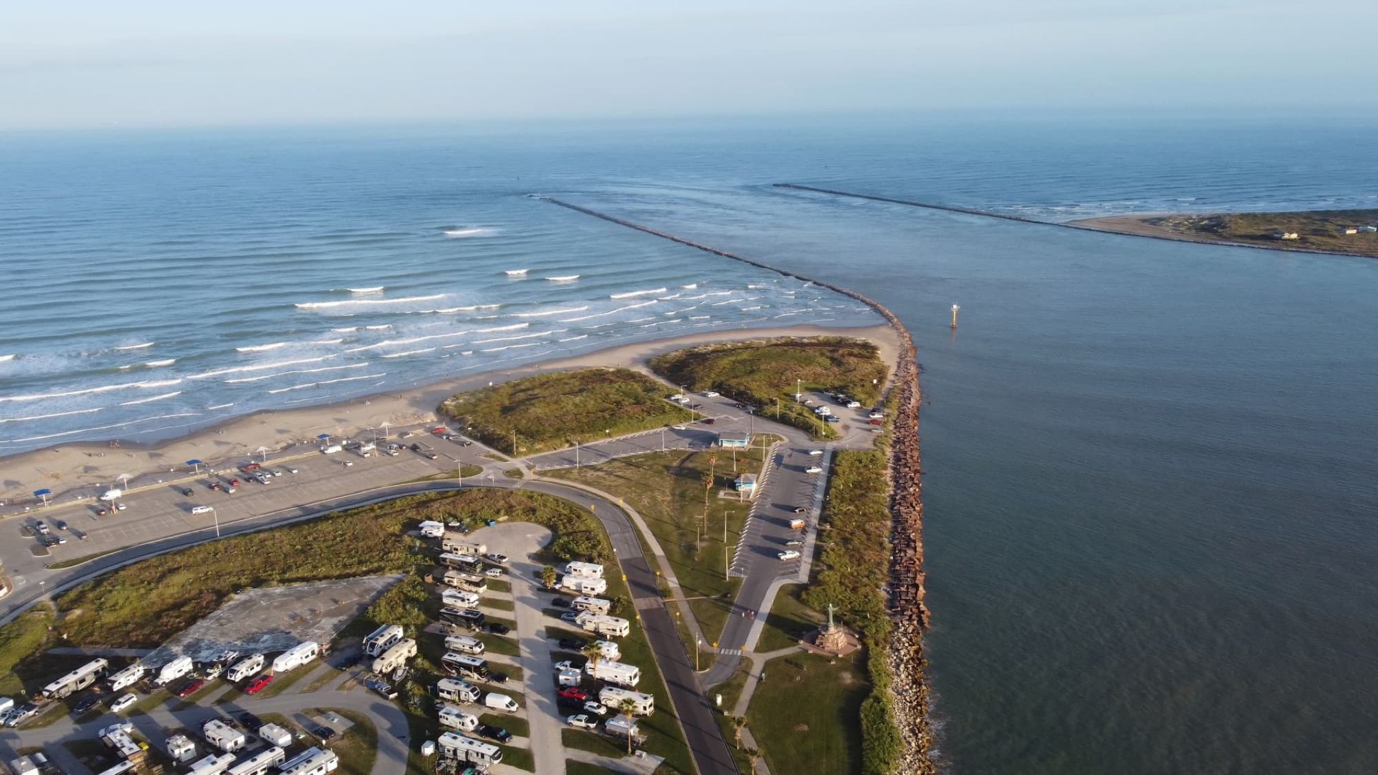 Drone view of a coastal camping site with ocean waves and scenic beach lines.