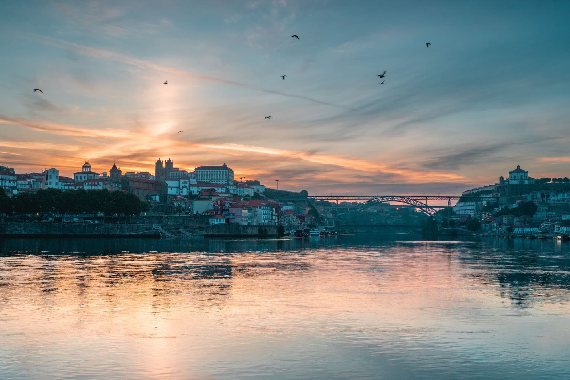 Beautiful sunset over the Douro River in Porto, Portugal, showcasing the city's skyline and bridge reflection.