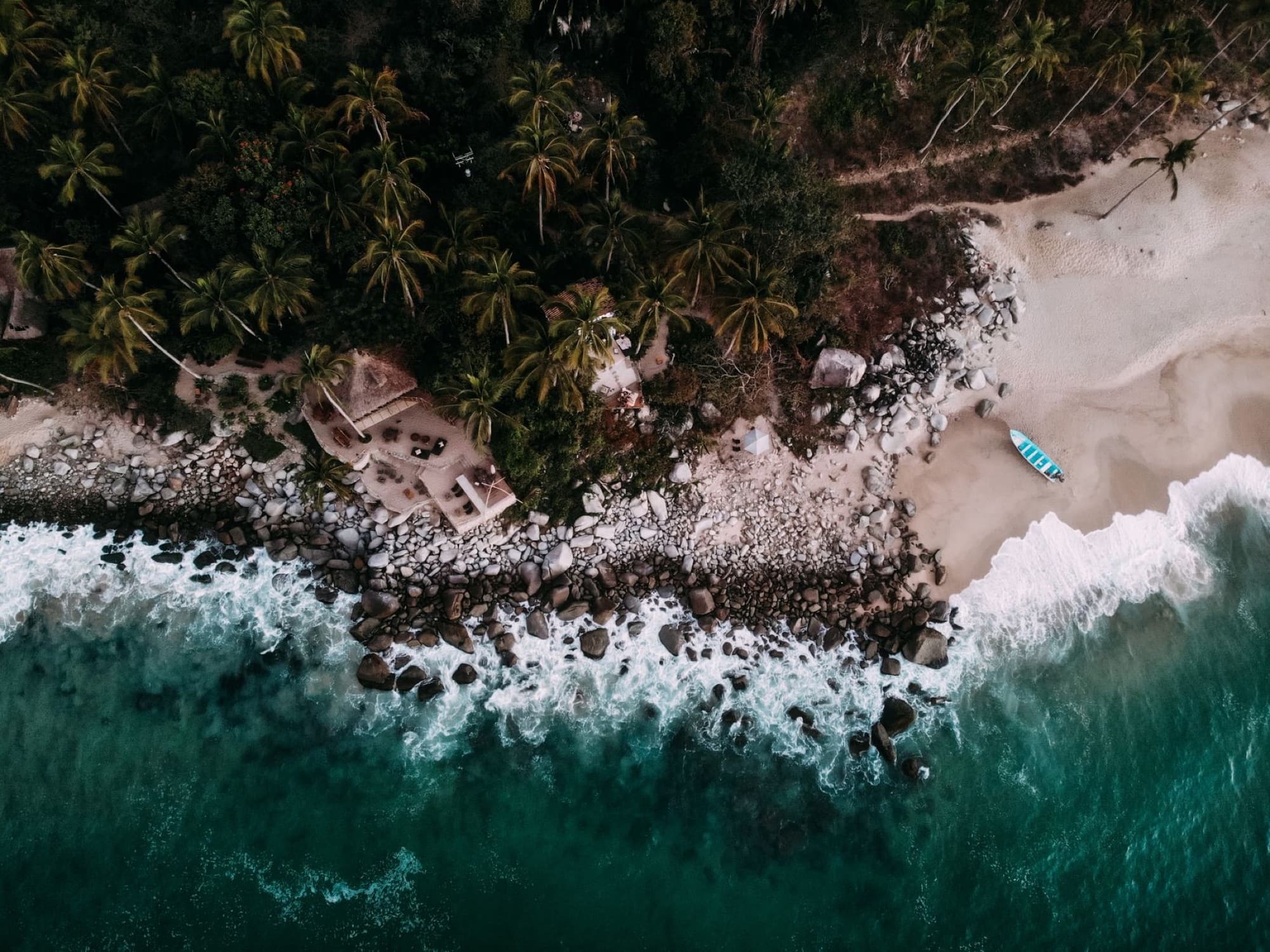 Drone shot of a scenic tropical beach in Mexico with palm trees and turquoise waves along the rocky shore.